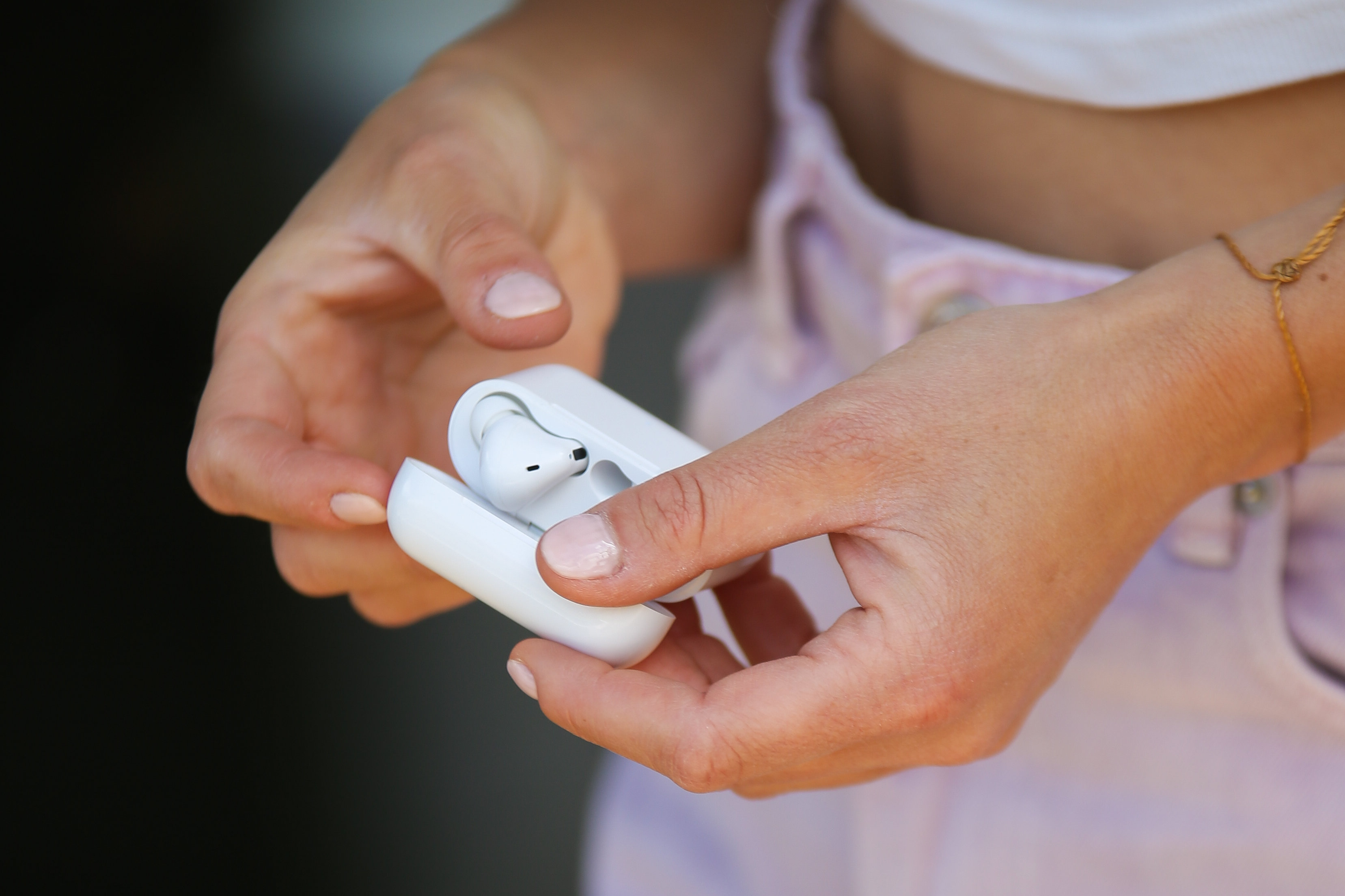 Osoba trzyma białe etui na słuchawki z wkładką douszną w środku. Osoba ma na sobie biały top i różowy kombinezon.