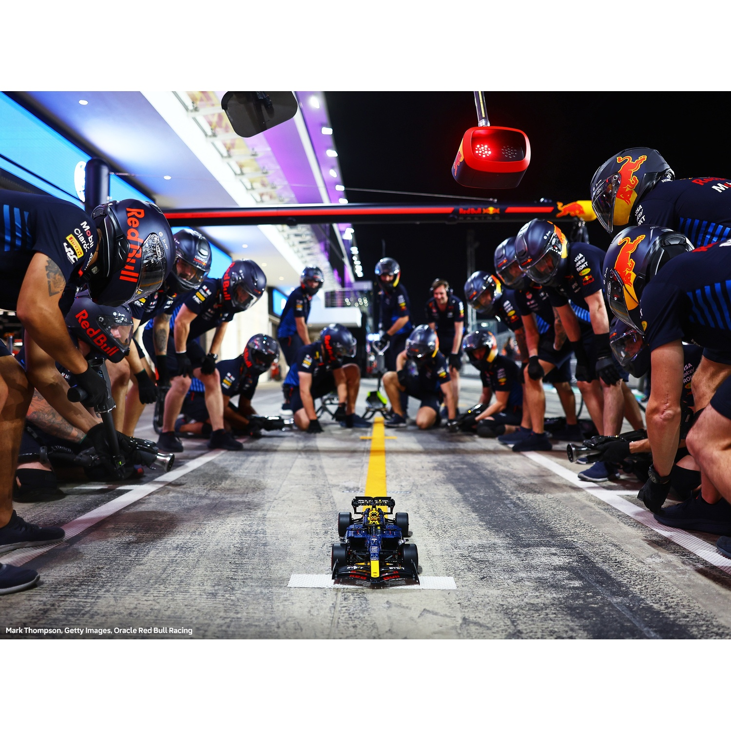 Una scena di pit stop di Formula 1. Un'auto da corsa è circondata da un team in uniforme Red Bull, pronto a riparare il veicolo.