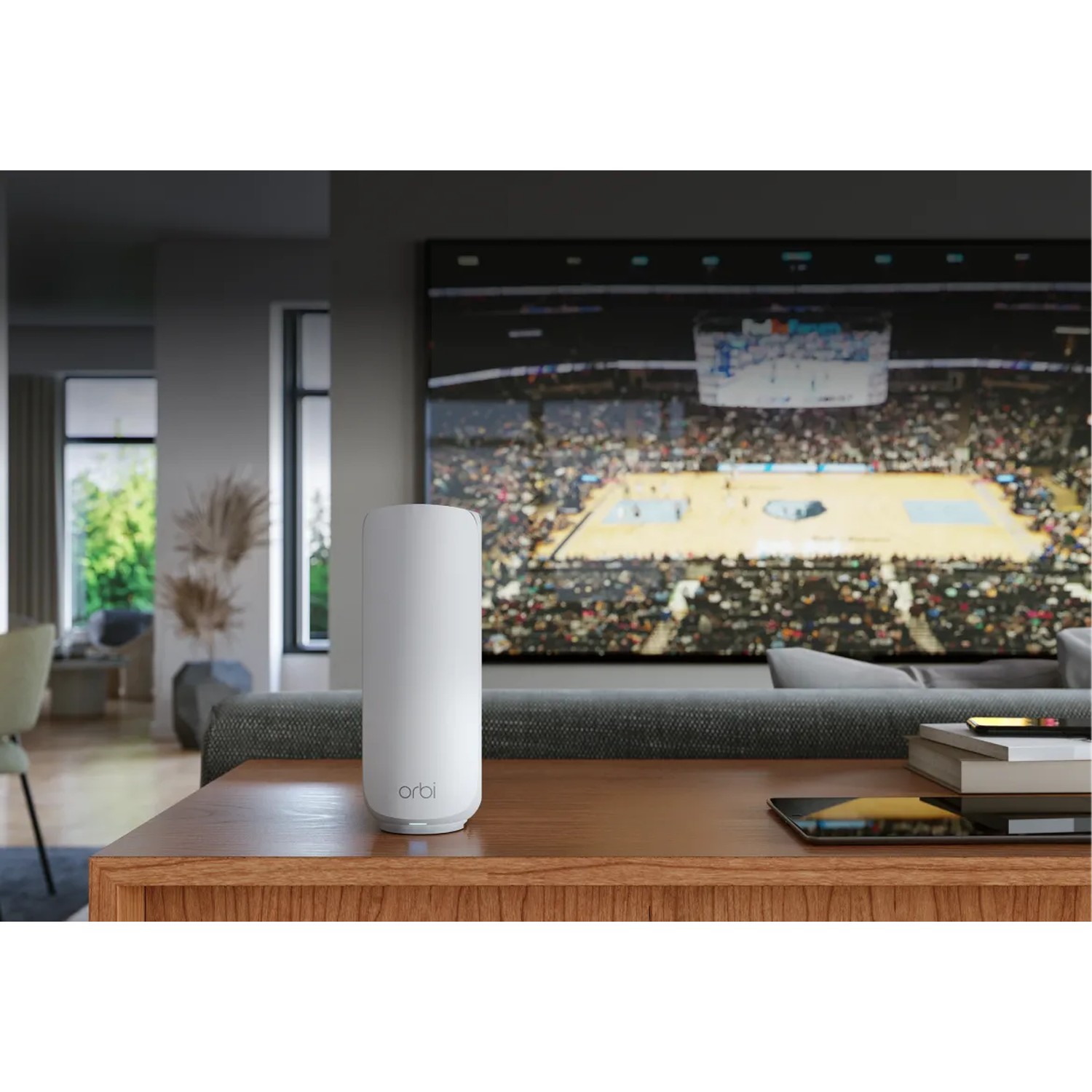 Un routeur blanc est posé sur une table en bois. Un grand téléviseur diffuse un match de basket. Un canapé et des éléments de décoration sont en arrière-plan.