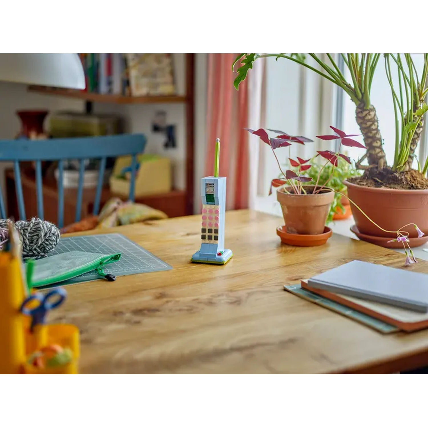 Un tavolo di legno con un telefono giocattolo, piante, libri e materiale per l'artigianato. Sfondo con sedia e libreria.