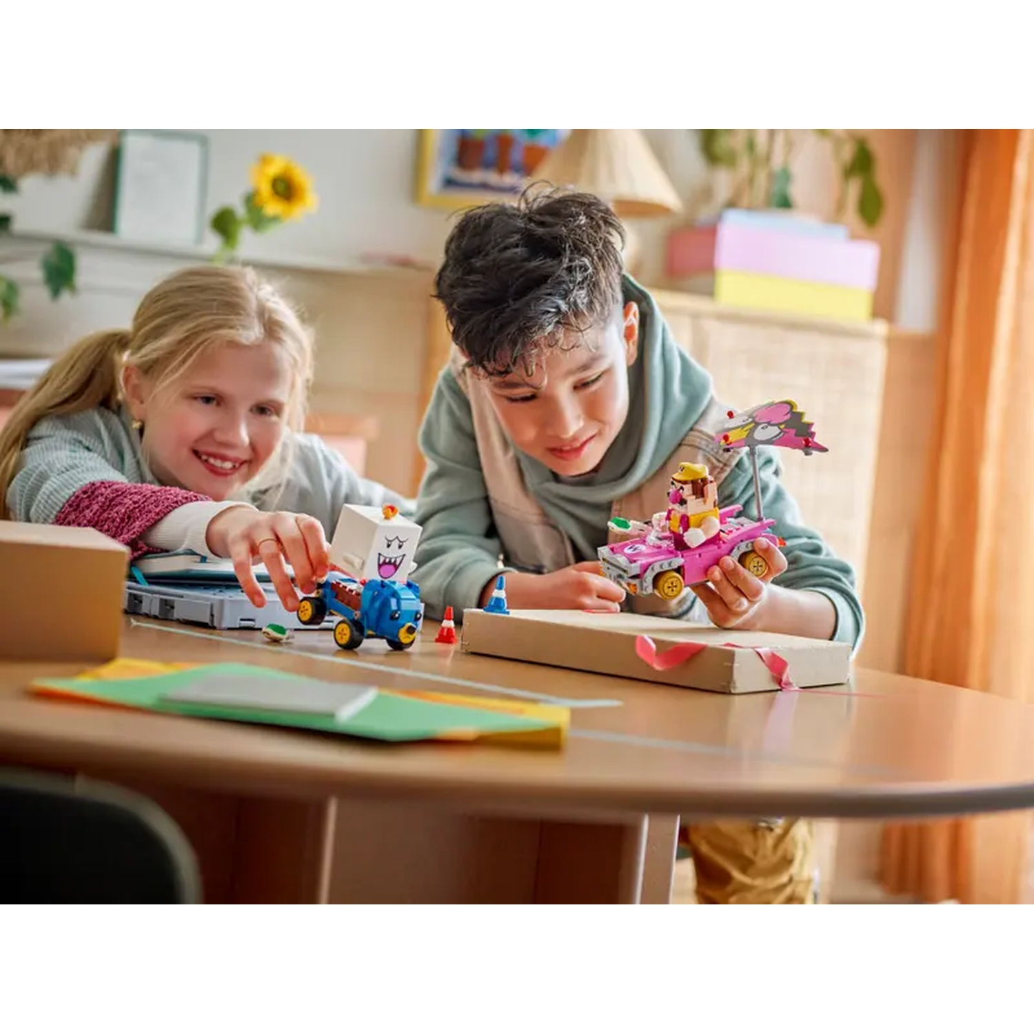 Due bambini che giocano con macchinine. Una bambina indica un'auto blu con un blocco bianco, l'altro bambino tiene un'auto rosa.