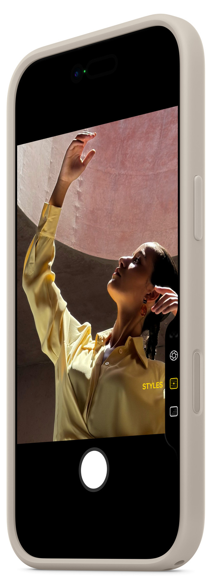 Kobieta w żółtej koszuli podnosi rękę. Obraz jest oprawiony przez telefon, wyświetlający widok z kamery.