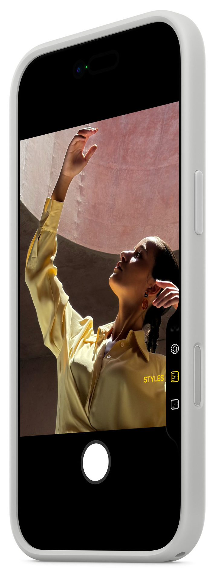 Kobieta w żółtej koszuli podnosi rękę. Trzyma telefon, widać widok z kamery.