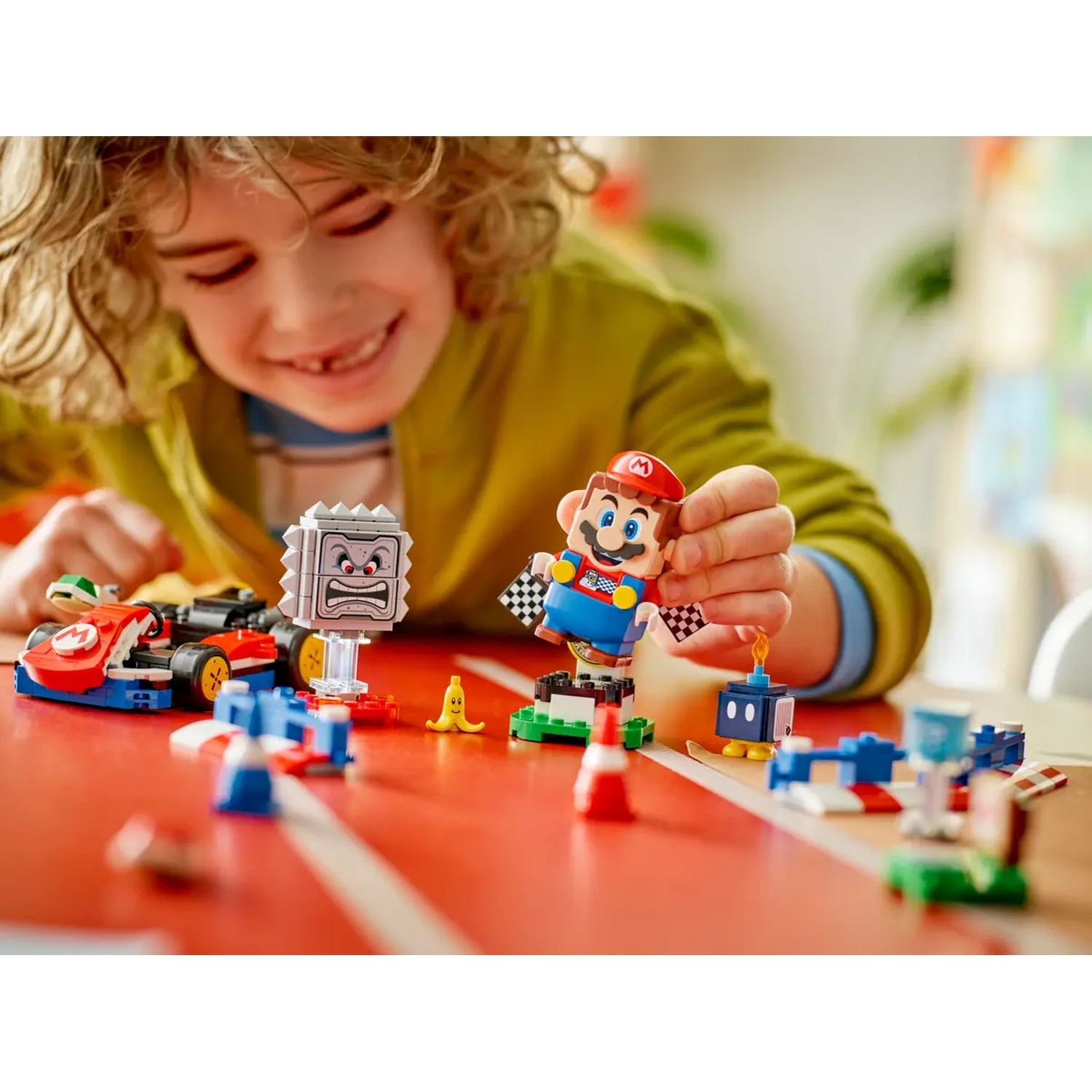 Un bambino tiene in mano un personaggio Lego di Mario. Il set Lego include un'auto da corsa, Thwomp, Bob-omb e altri elementi della pista.