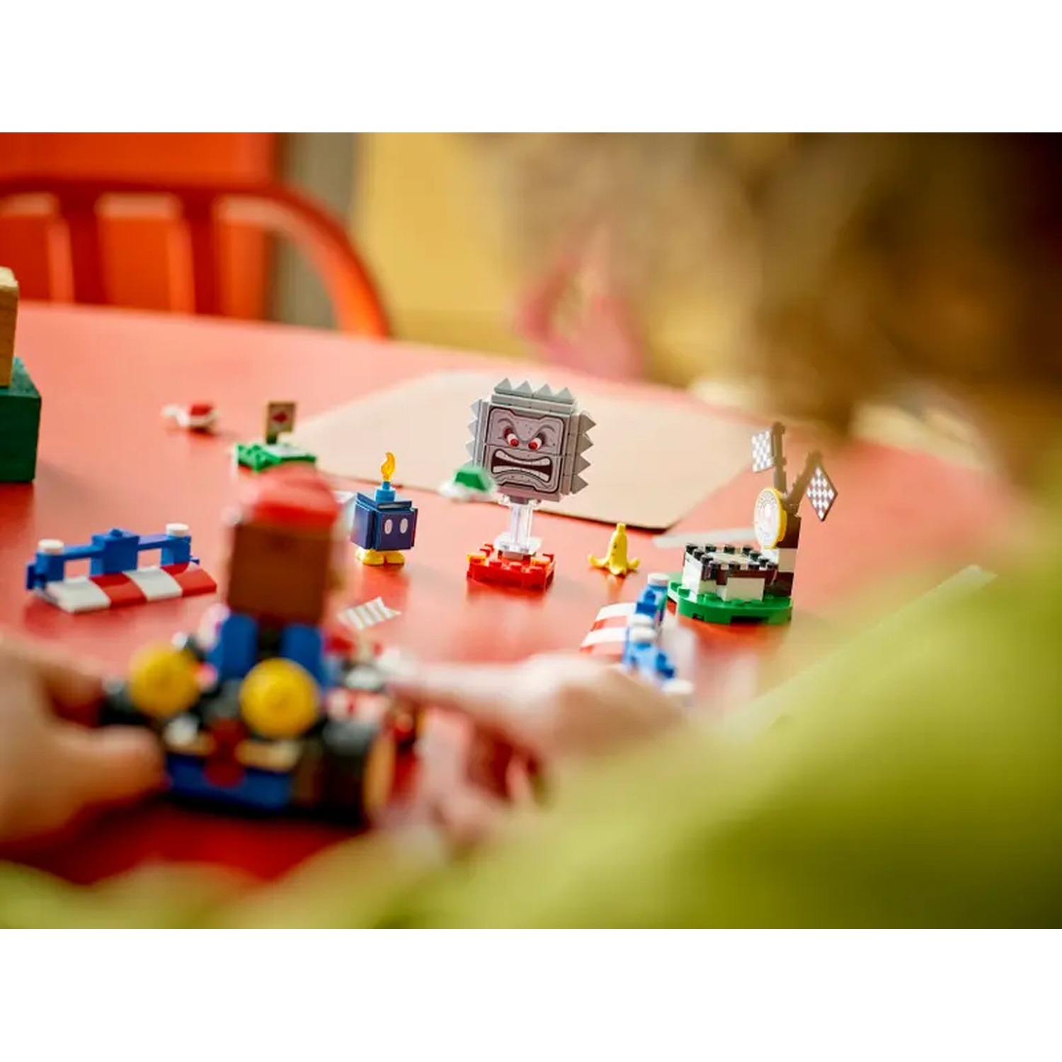 Una persona gioca con i set Lego Mario Kart su un tavolo rosso. Sono visibili diversi personaggi e oggetti Lego.