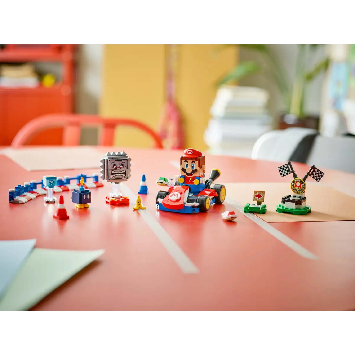 Un set Lego Mario kart è su un tavolo rosso. Include Mario in un kart, Thwomp, ostacoli e un traguardo.