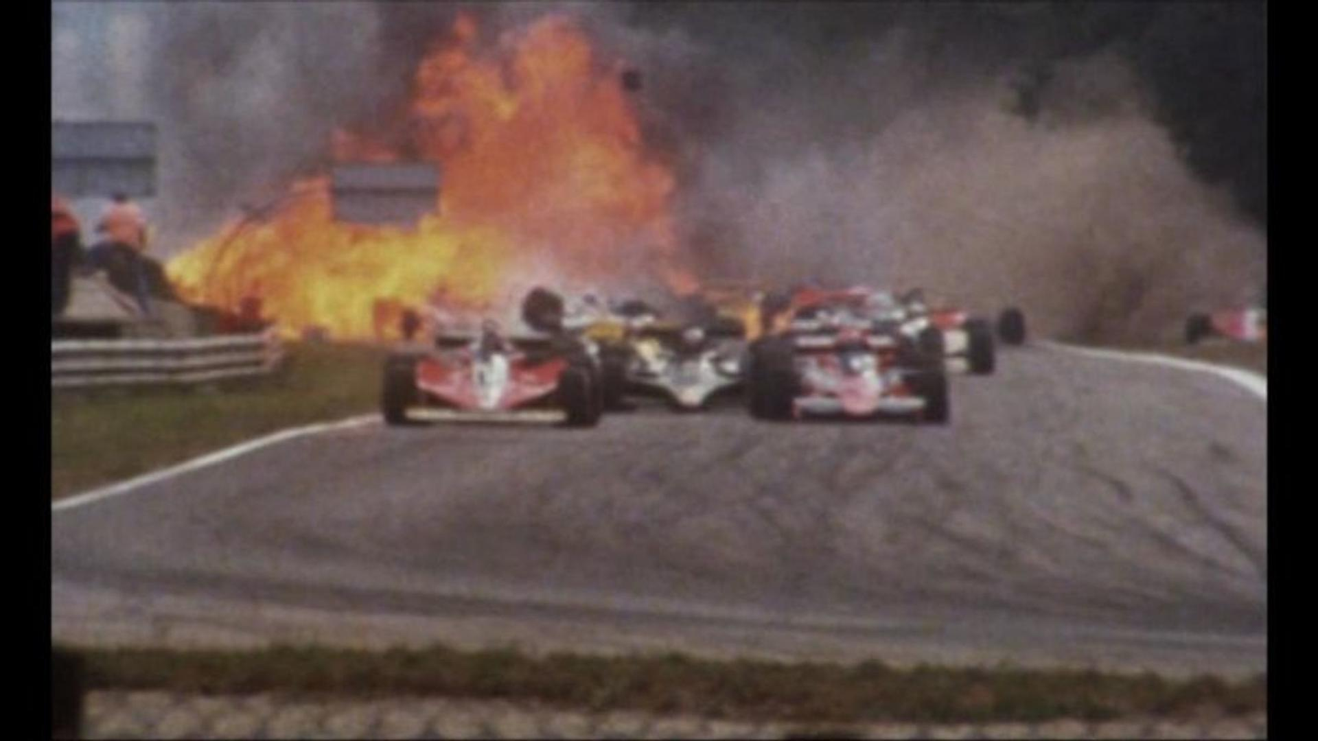 Rennwagen auf der Strecke mit Feuer im Hintergrund. Mehrere Autos rasen, mit großem Feuer und Rauch.