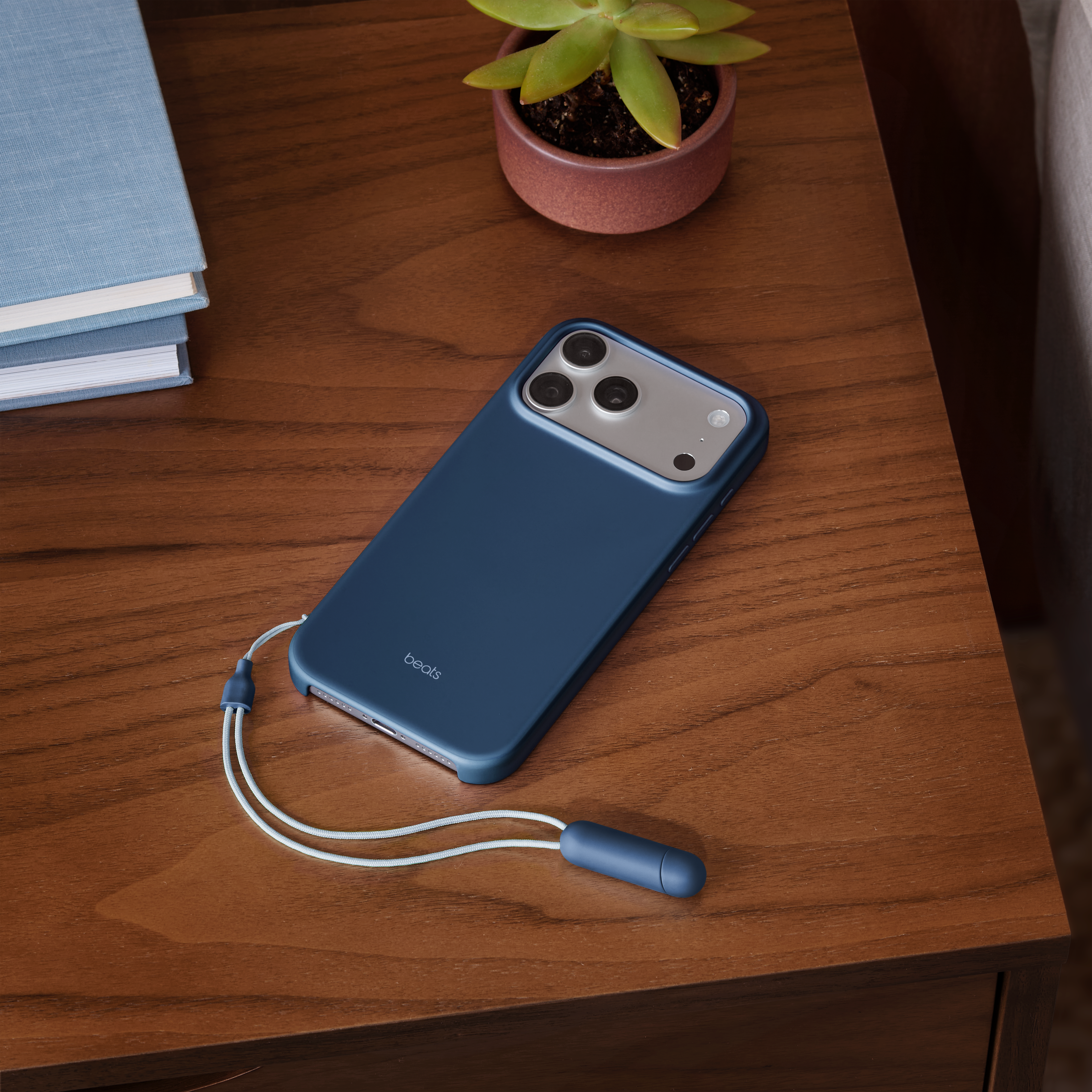 Un étui de téléphone bleu avec un cordon sur une table en bois. Une plante et des livres sont également présents.