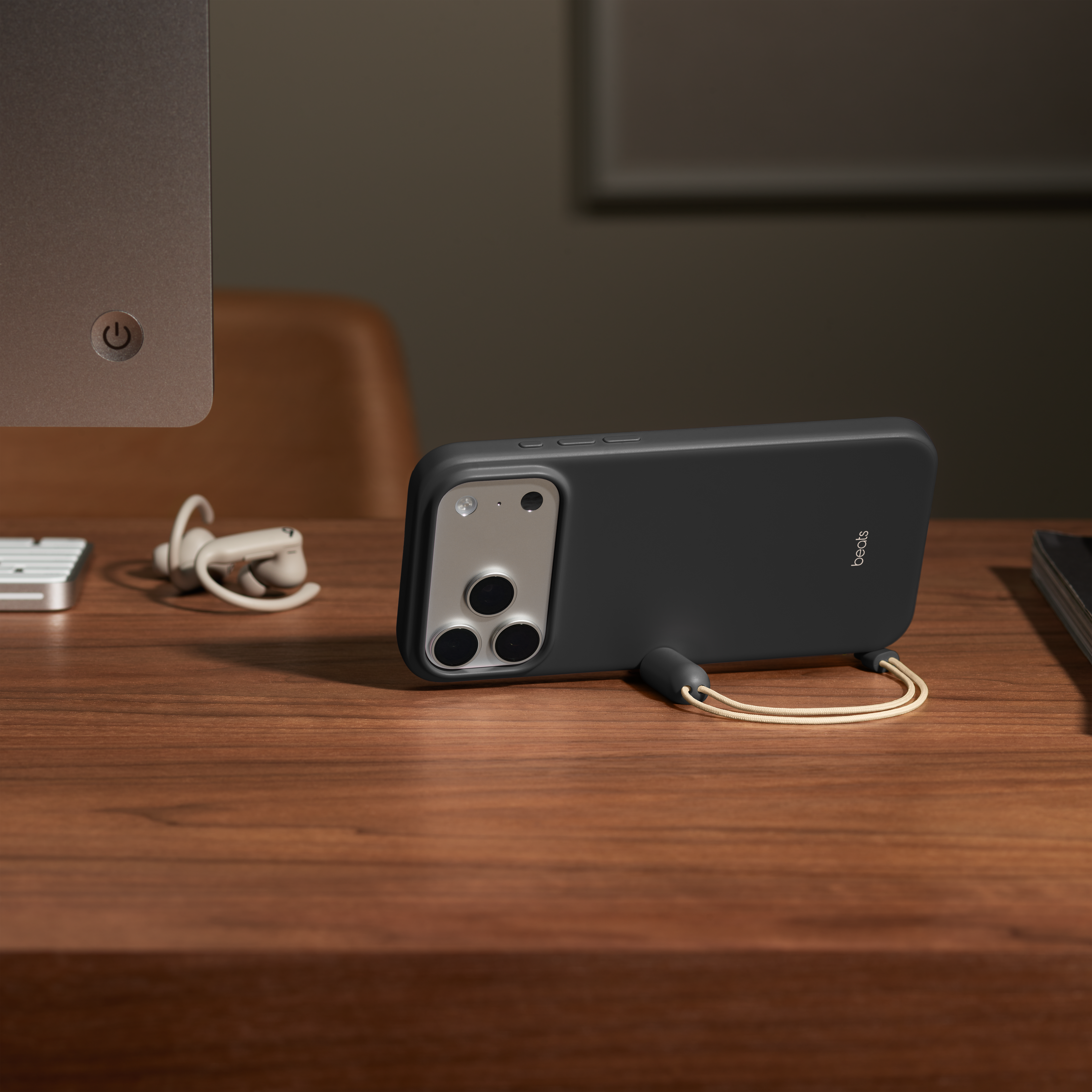 Un téléphone noir dans un étui repose sur un bureau en bois. Des écouteurs et un ordinateur sont également visibles.