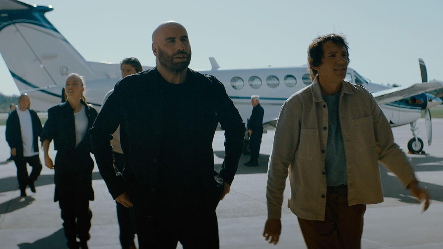 Männer gehen an einem sonnigen Tag in der Nähe eines kleinen Flugzeugs spazieren. Ein Mann in Schwarz, ein anderer in einer leichten Jacke.