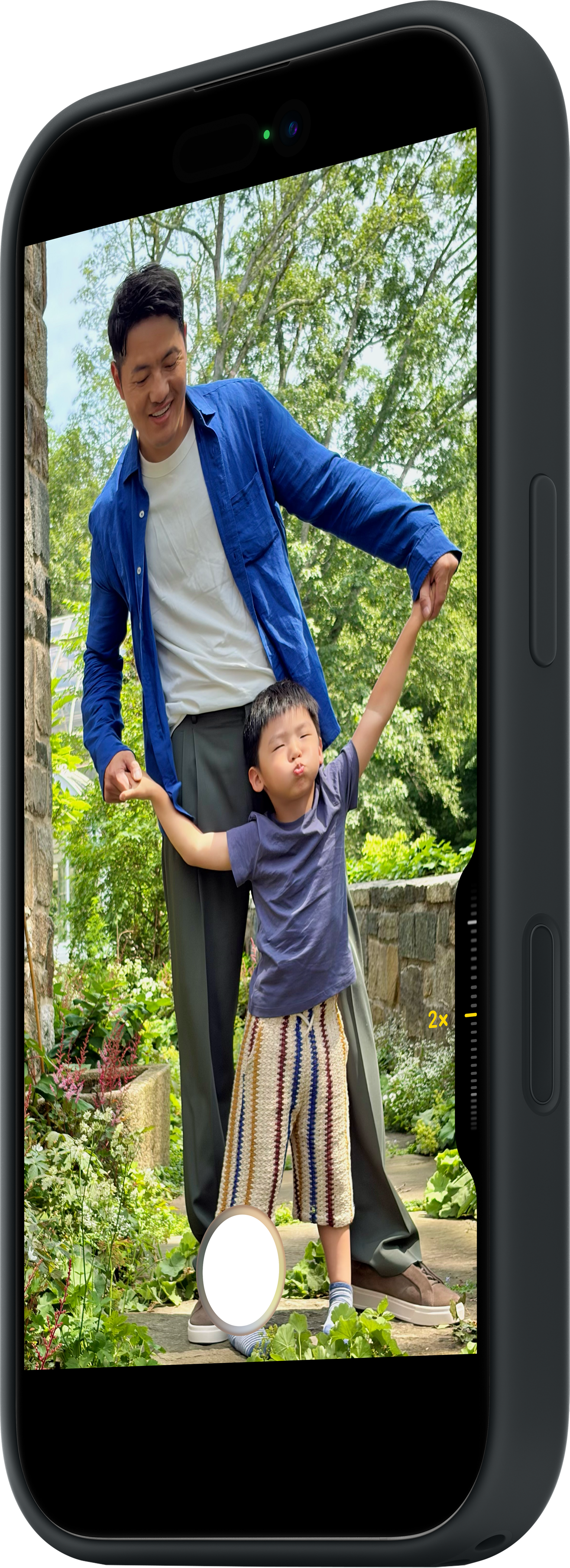 Ein Mann und ein Junge halten sich in einem Garten an den Händen. Der Junge hat die Arme oben und macht ein Gesicht. Der Mann lächelt.