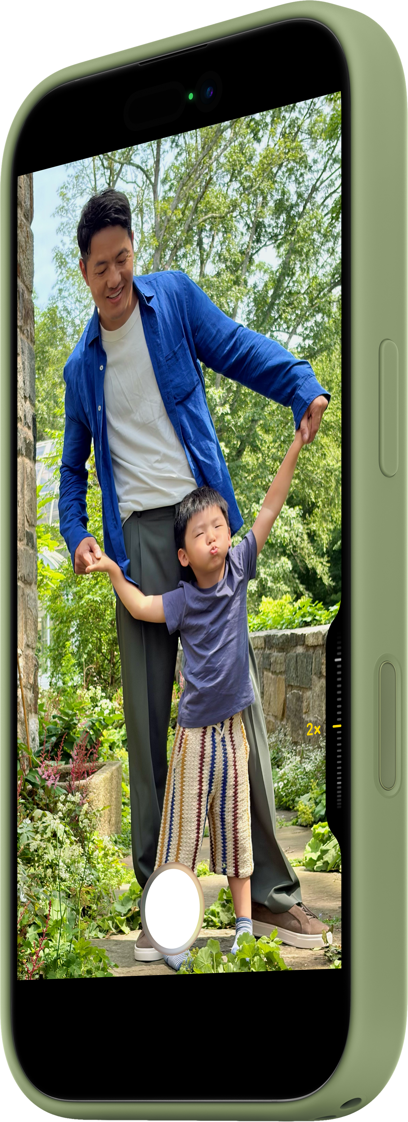 Un uomo in camicia blu tiene le mani di un bambino in alto. Sono in un giardino. Il bambino indossa pantaloncini colorati.