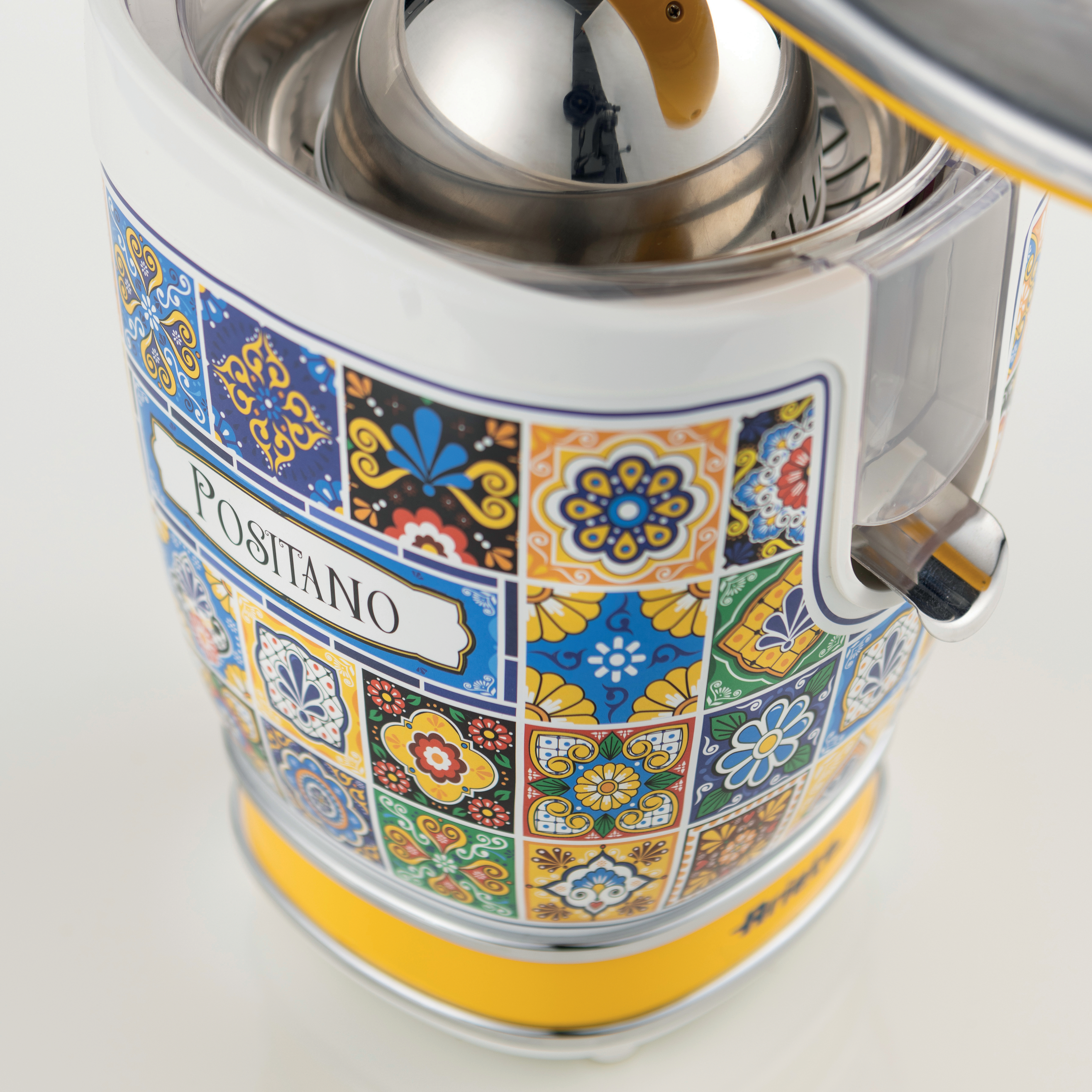 Nahaufnahme einer Zitruspresse. Sie hat ein farbenfrohes Kacheldesign mit dem Wort "POSITANO". Der Sockel ist gelb und die Innenteile sind silbern.