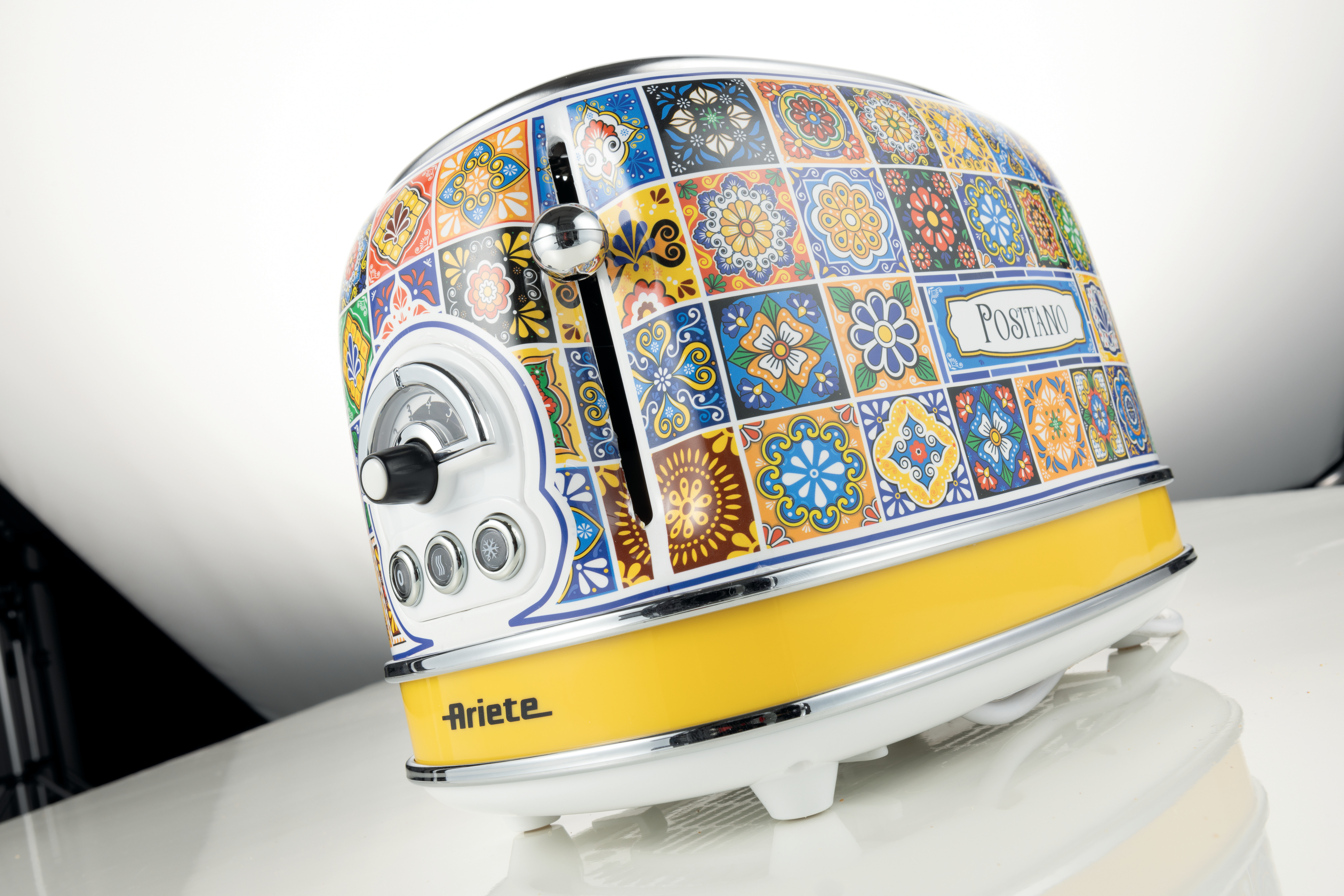 Ein bunter Toaster mit Mosaikmuster, gelbem Sockel, Chromakzenten und dem Wort "Positano" auf der Seite.