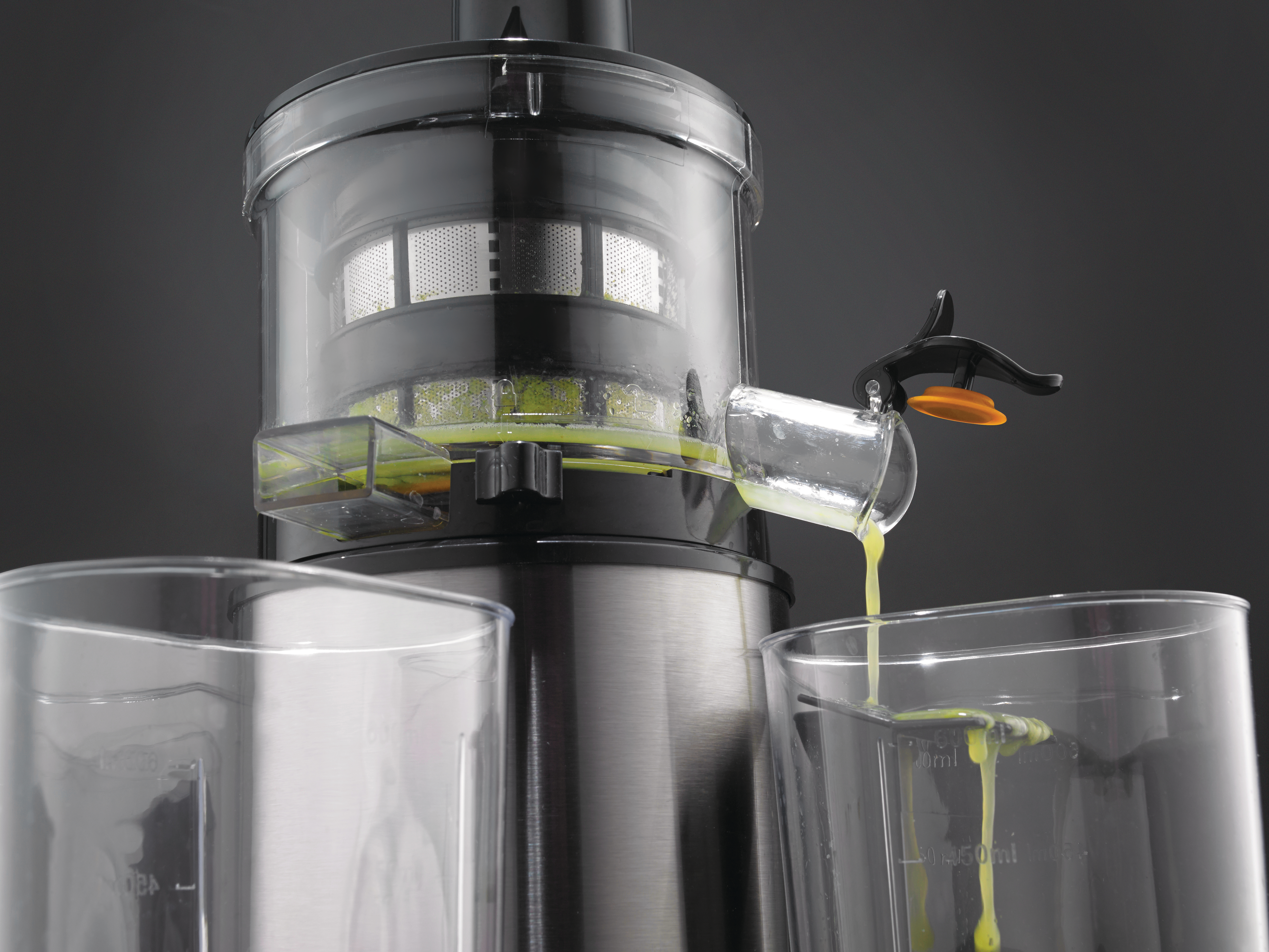 Entsafter, Saft fließt in ein Glas. Der Entsafter ist silber und schwarz, mit transparenten Teilen. Zwei Gläser stehen davor.