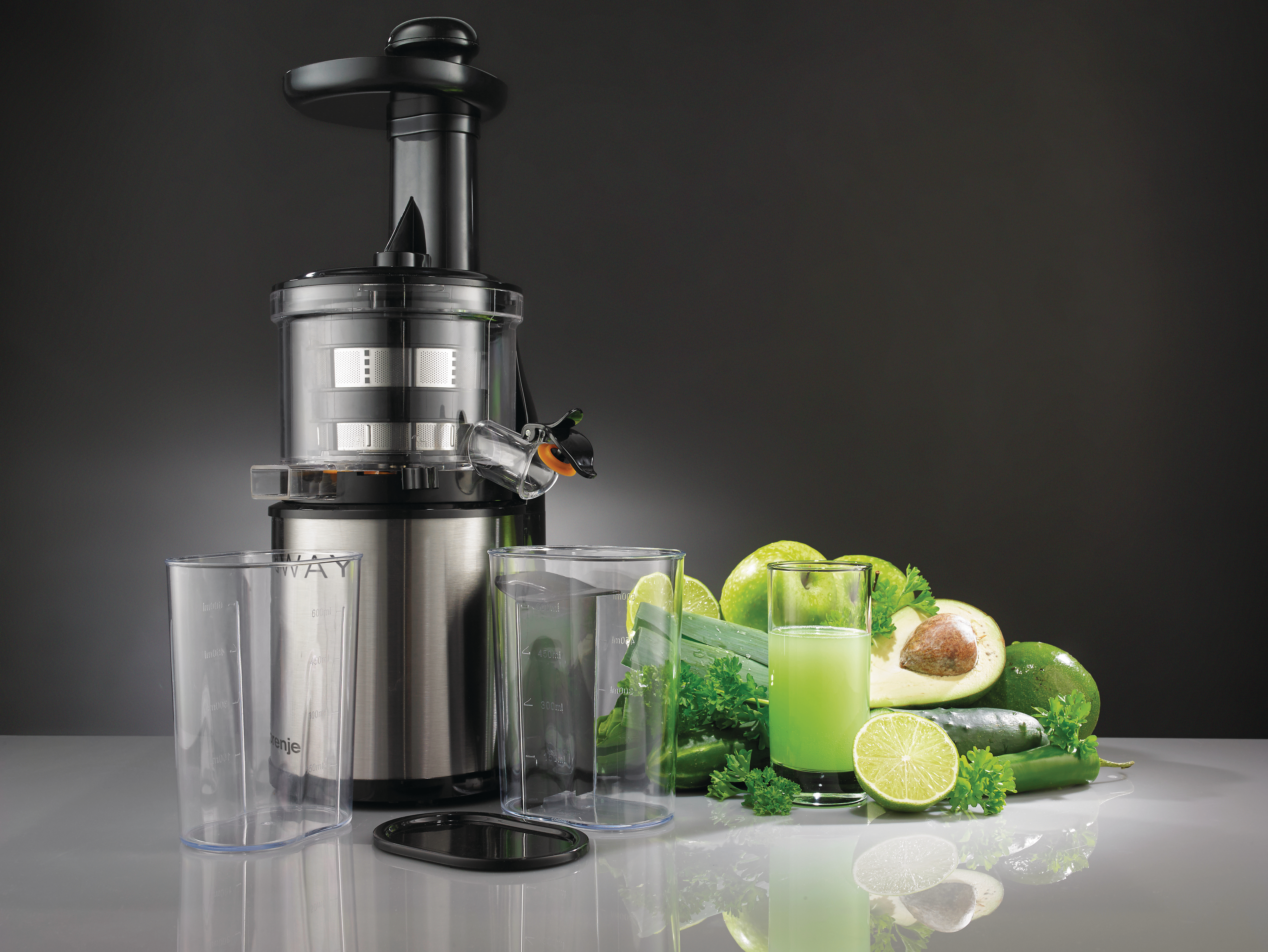 Ein Entsafter mit Obst und Gemüse. Beinhaltet grüne Äpfel, Limetten, Avocado und ein Glas Saft.