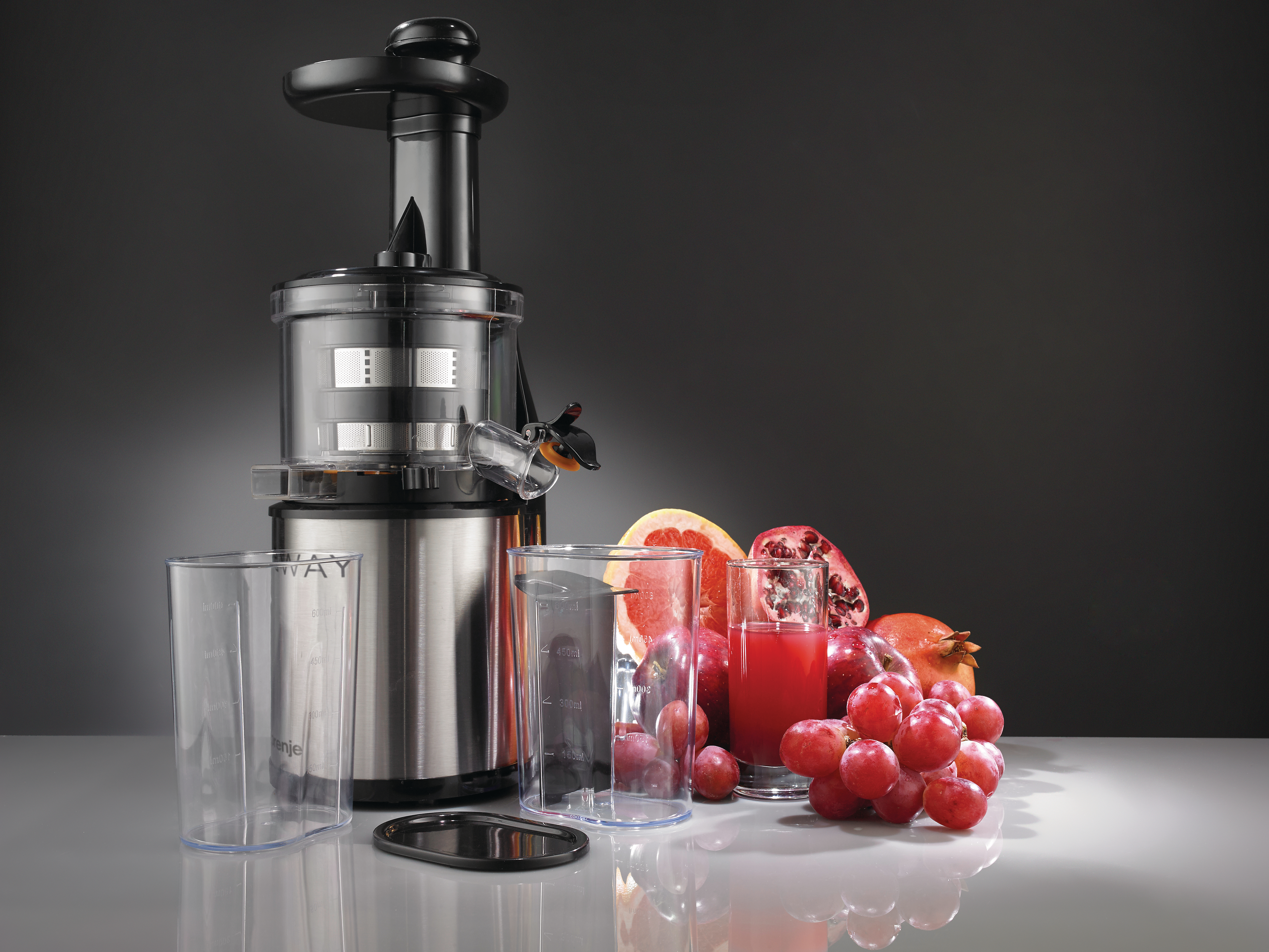 Ein Entsafter mit Gläsern, Früchte wie Granatapfel, Grapefruit und Trauben liegen auf dem Tisch. Ein Glas Saft ist ebenfalls vorhanden.
