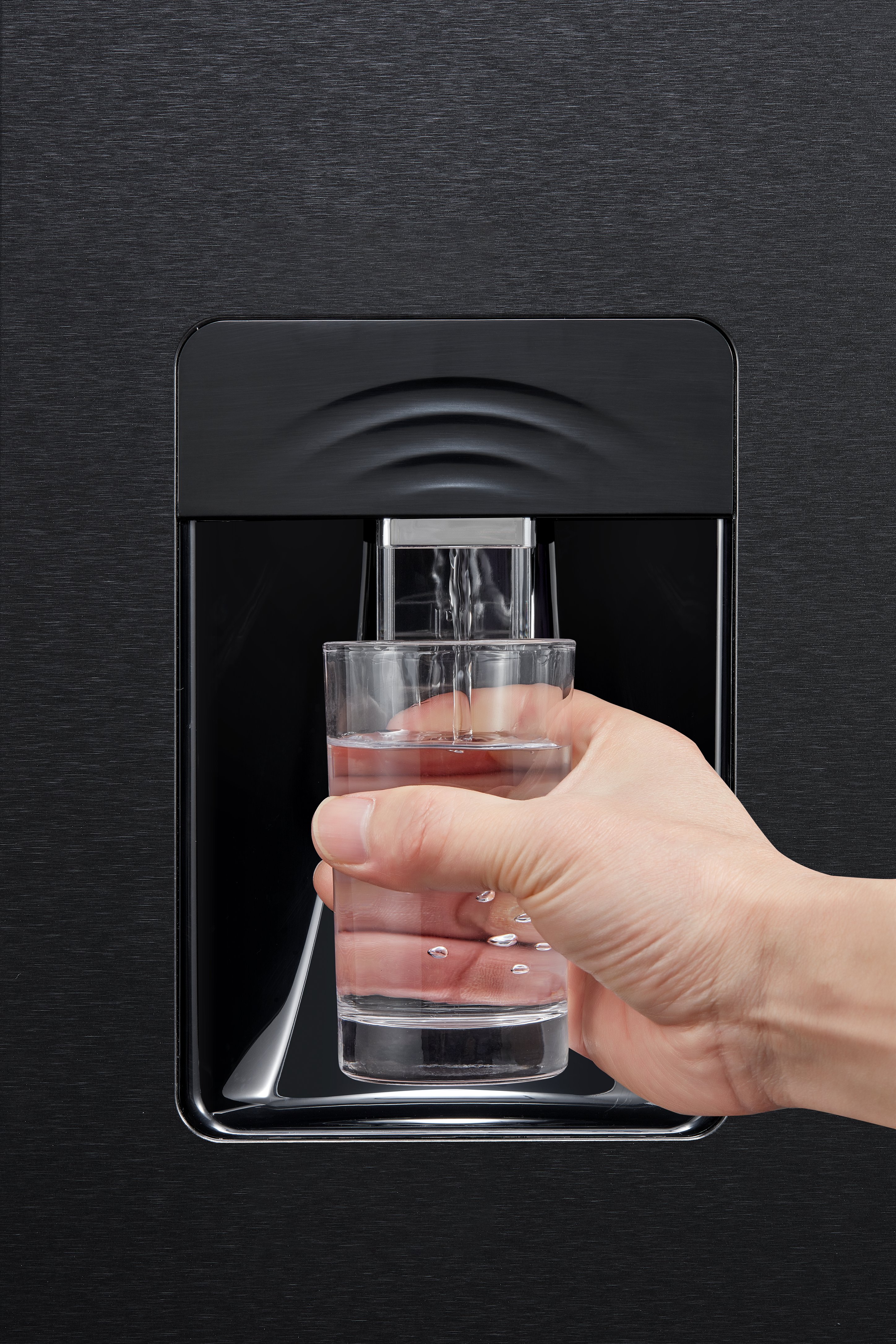 Eine Hand hält ein Glas, das sich mit Wasser aus einem schwarzen Spender füllt. Wassertropfen sind sichtbar.