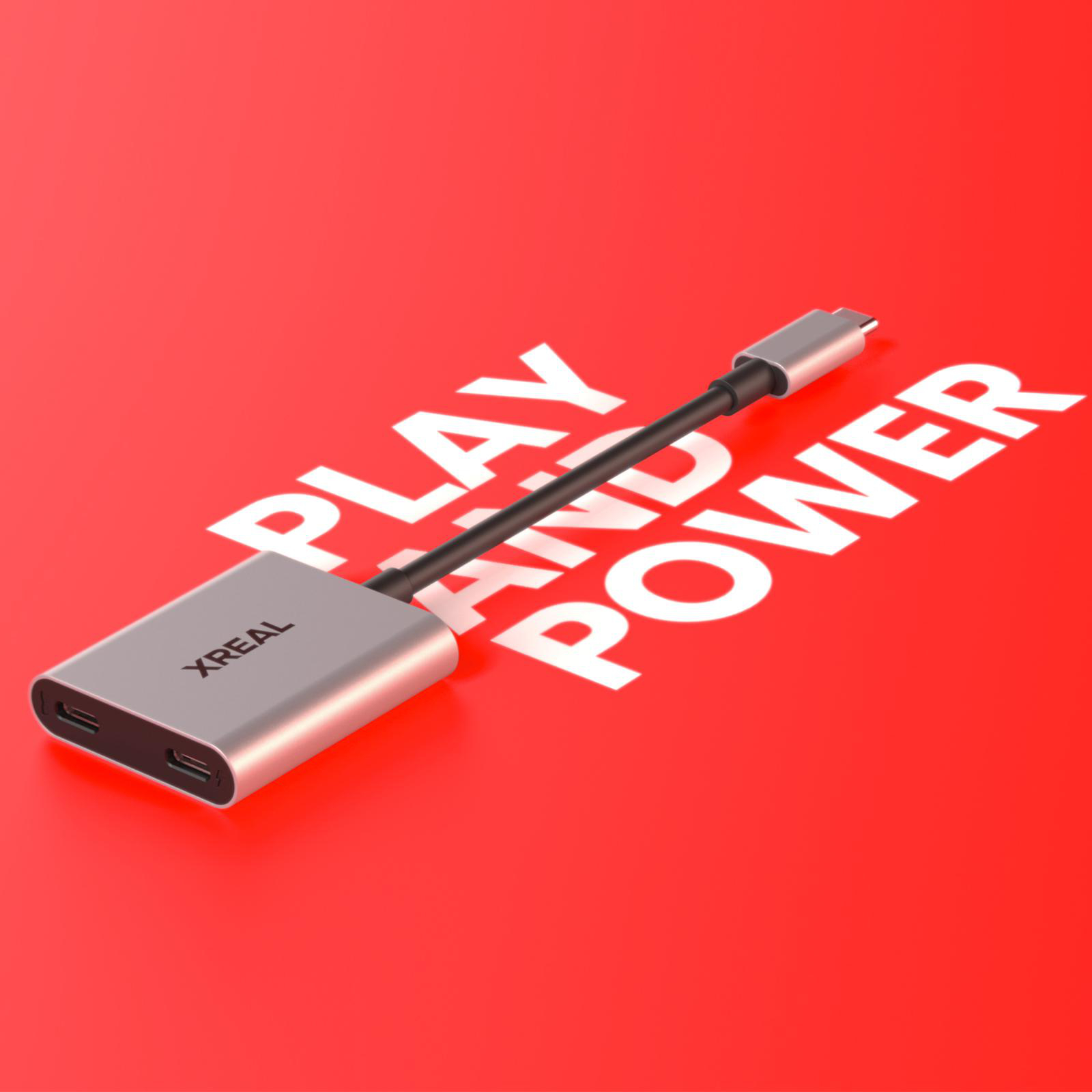 Silberner Adapter mit schwarzem Kabel auf rotem Hintergrund mit weißem Text: PLAY AND POWER. Marke XREAL sichtbar.