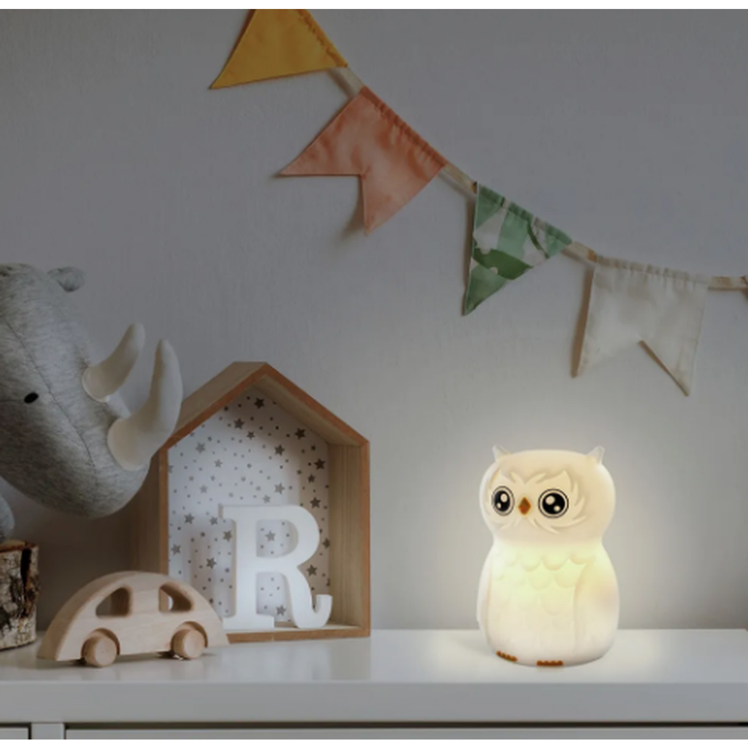 An owl-shaped night light sits on a shelf. A wooden car, a rhino toy, and a house-shaped shelf are also on the shelf.
