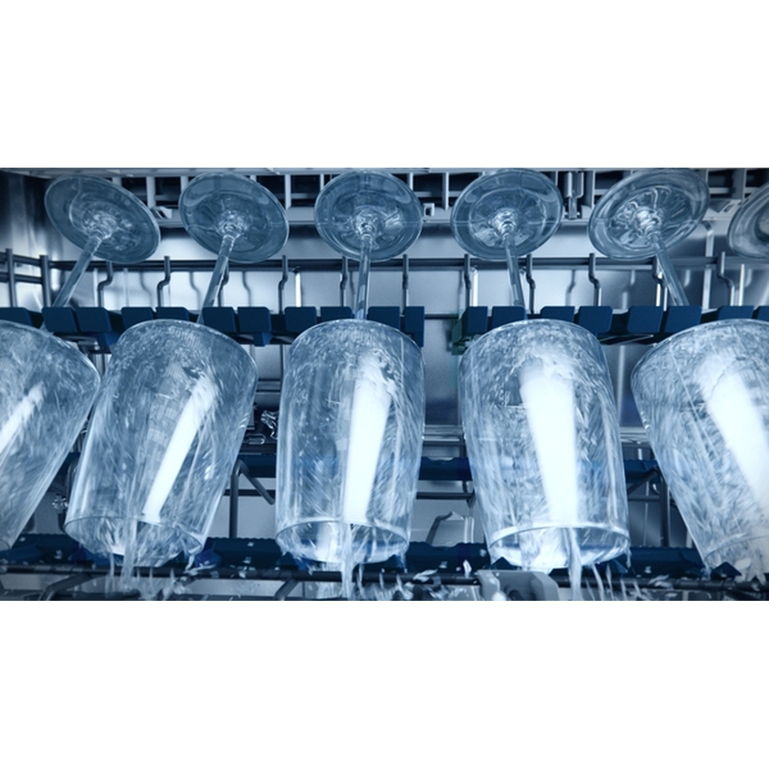 À l'intérieur d'un lave-vaisselle, plusieurs verres à vin transparents sont à l'envers. L'eau s'en échappe. La scène est éclairée de tons froids.