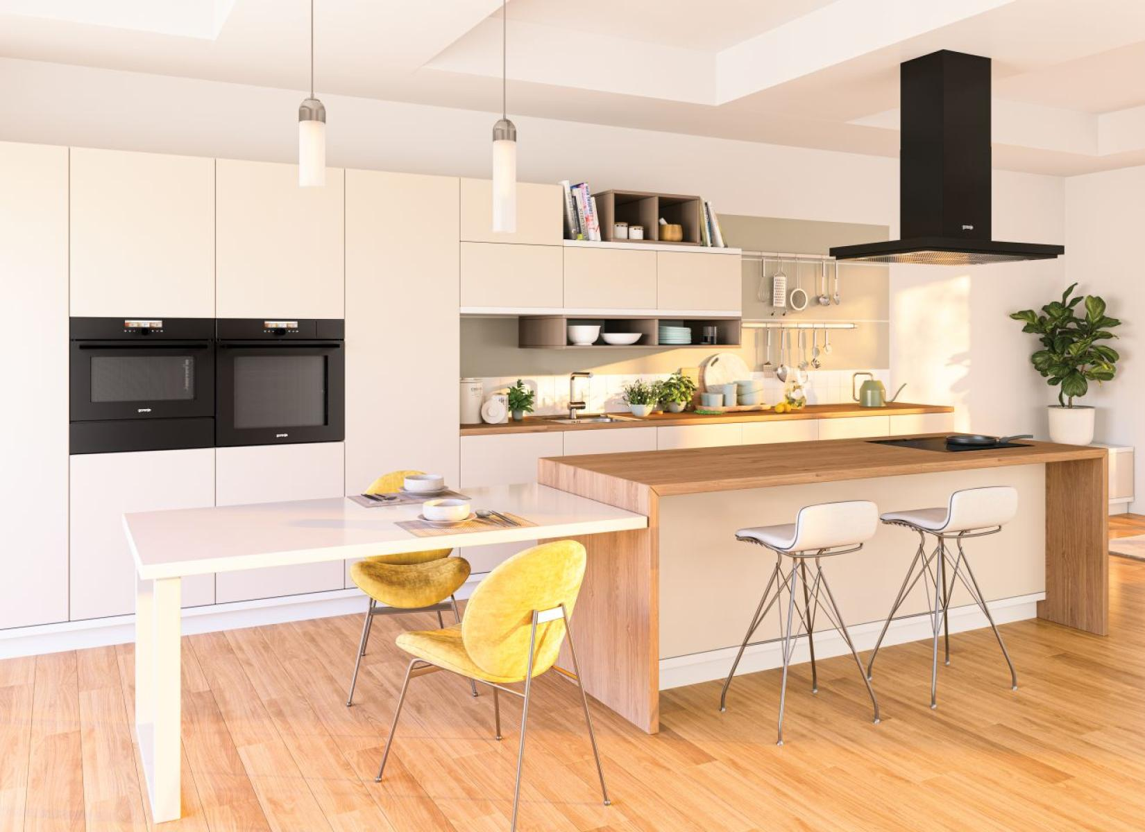 Nowoczesna kuchnia z białymi szafkami, drewnianą wyspą i stołem jadalnym. Zawiera piekarniki, krzesła i zieloną roślinę.