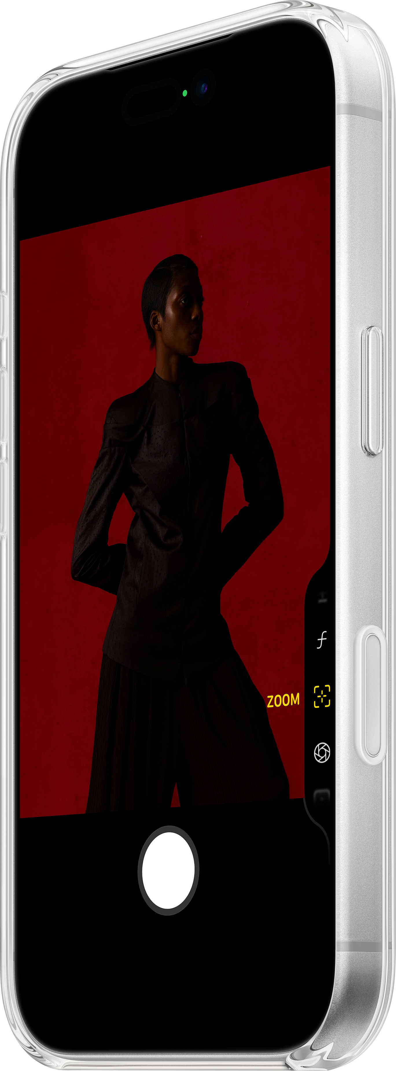 Une personne en vêtements sombres se tient devant un fond rouge, encadrée dans un téléphone. Le téléphone affiche les commandes de l'appareil photo.