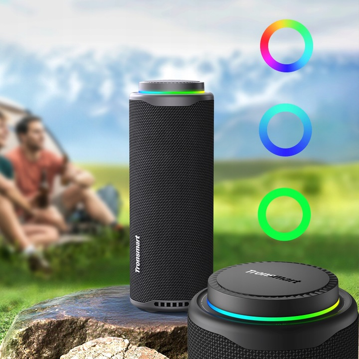 Czarny głośnik Tronsmart z kolorowymi światłami, drugi głośnik, dwie osoby i namiot w tle, scena na zewnątrz.
