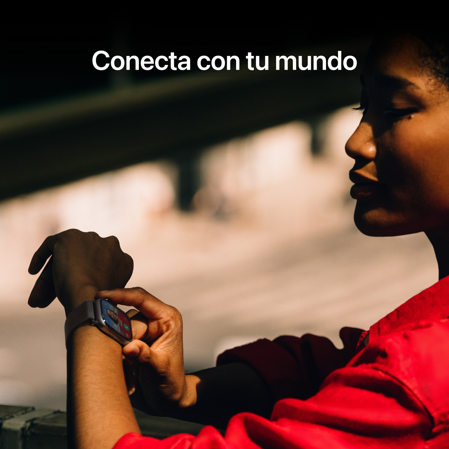 Una mujer con camisa roja mira su Apple Watch, mostrando una videollamada. El fondo muestra una escena borrosa al aire libre.