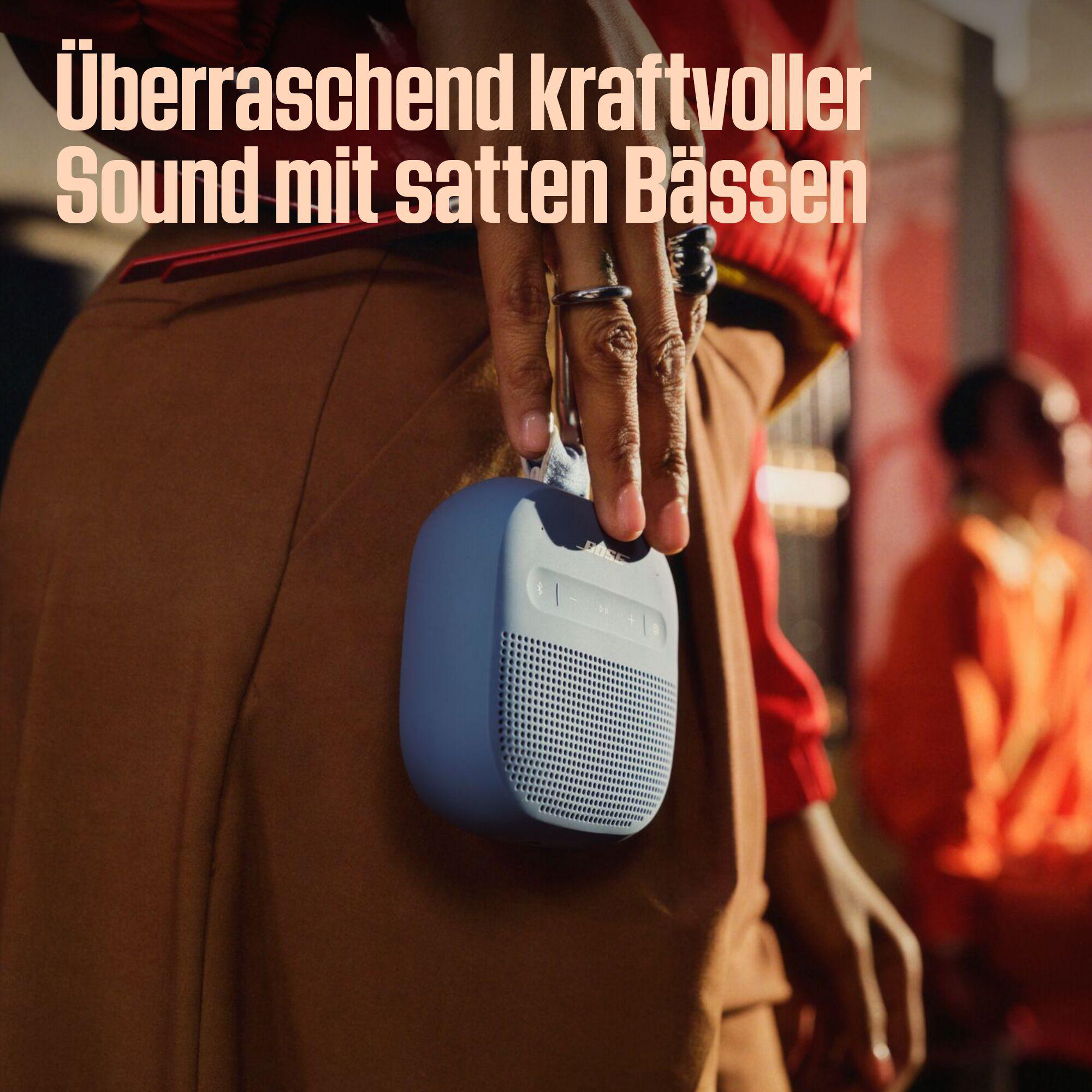 Eine Person hält einen blauen Lautsprecher. Text auf Deutsch lautet: 'Überraschend kraftvoller Sound mit satten Bässen'.