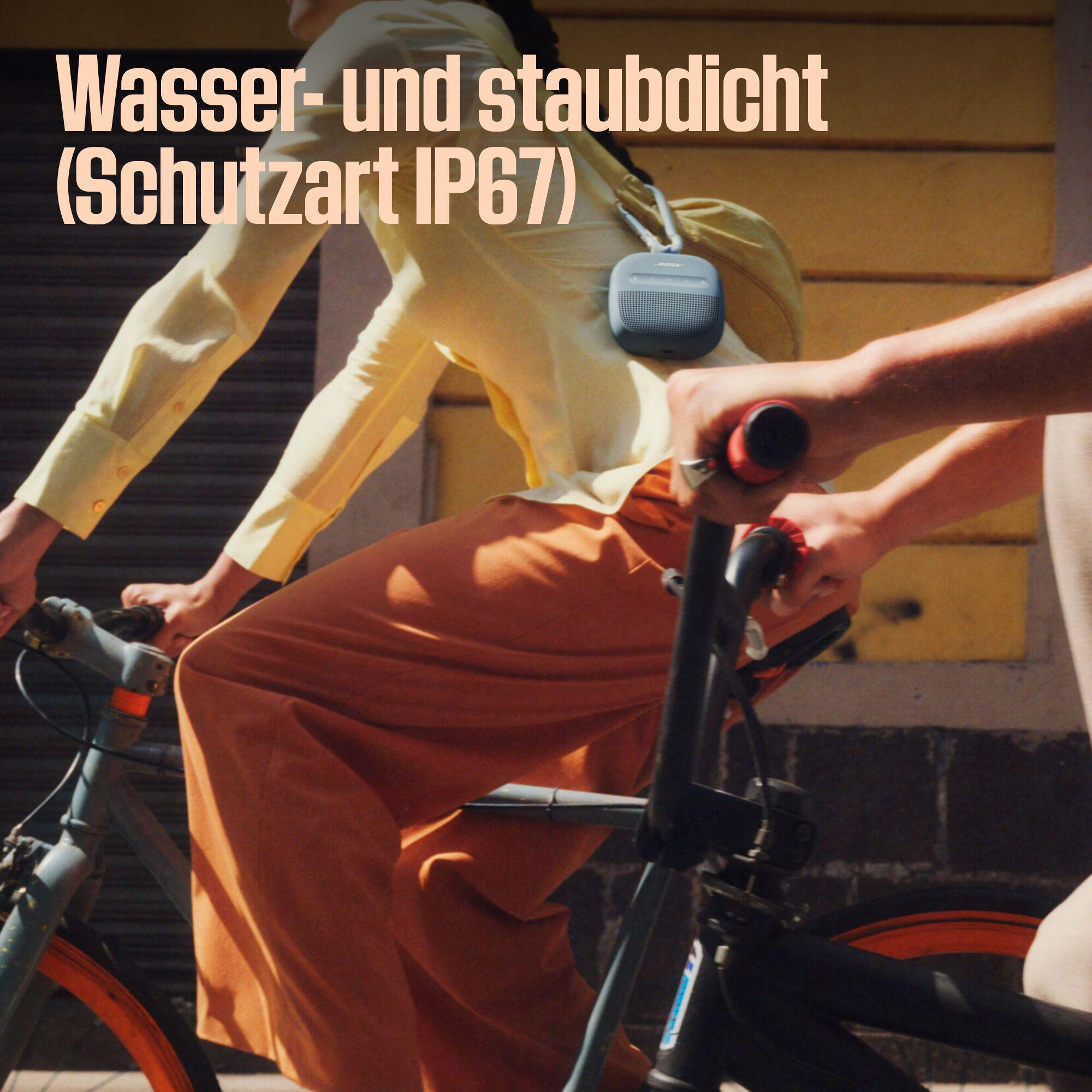 Person fährt Fahrrad, trägt gelbes Hemd und orangefarbene Hose. Kleiner Lautsprecher auf der Schulter. Das Fahrrad ist blau.