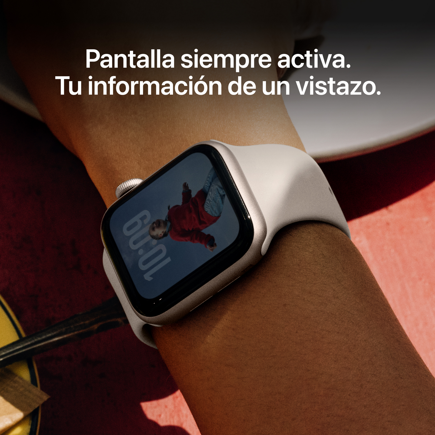 Muñeca de una persona con un Apple Watch blanco. El reloj muestra una persona y la hora 10:09. El fondo es rojo y blanco.