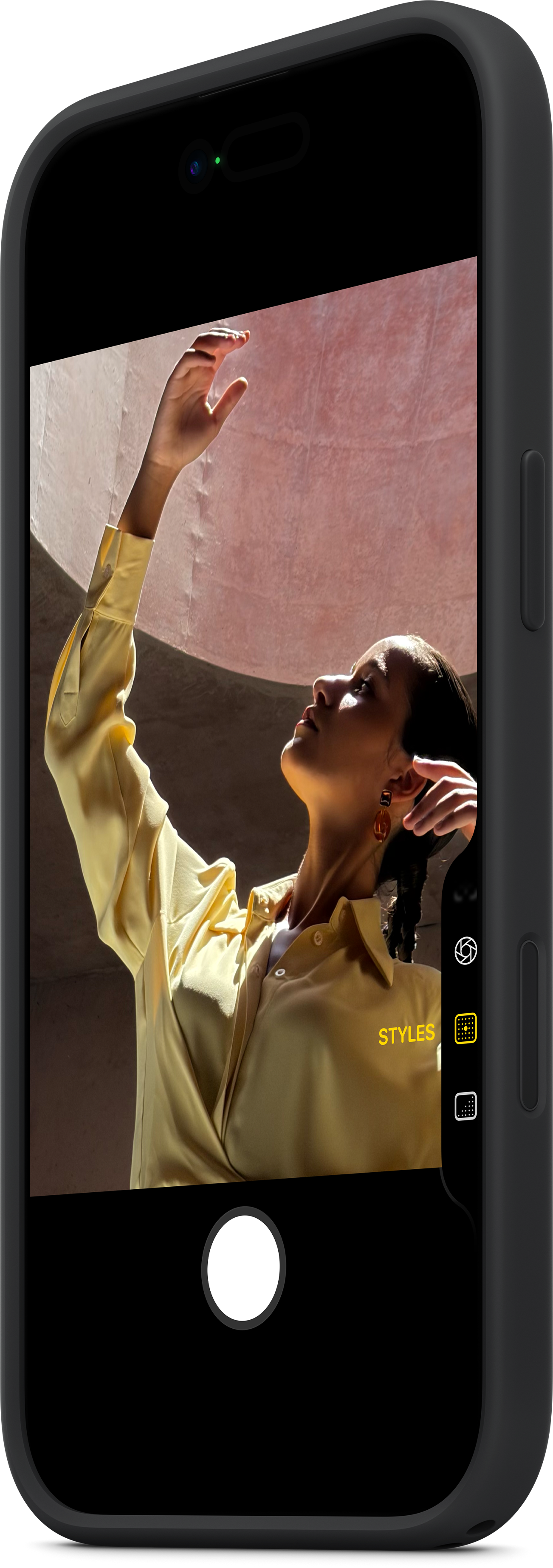 Eine Person in gelbem Hemd hält die Hand hoch. Das Foto wird mit einem Telefon aufgenommen. Der Hintergrund ist rosa.