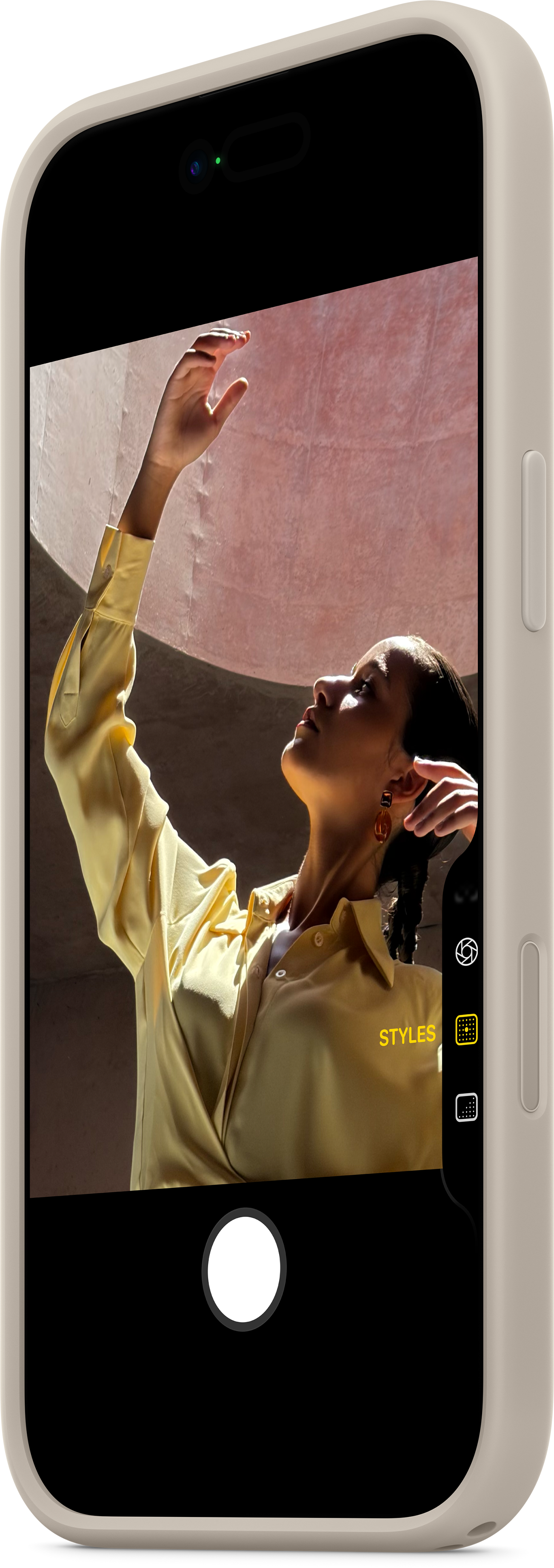 Eine Frau im gelben Hemd hebt den Arm und blickt nach oben. Der Hintergrund ist eine rosa Wand. Bild mit einem Telefon aufgenommen.