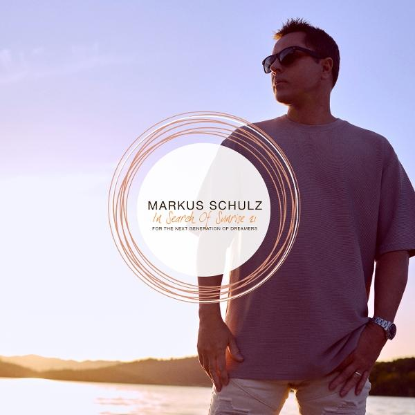 Mann mit Sonnenbrille steht am Wasser. Text in einem Kreis: Markus Schulz In Search Of Sunrise 21. Für die nächste Generation von Träumern.