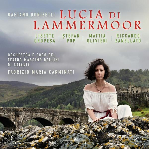 Eine Frau in weißem Kleid sitzt auf Felsen, Brücke und Burg im Hintergrund. Text: "Lucia di Lammermoor".