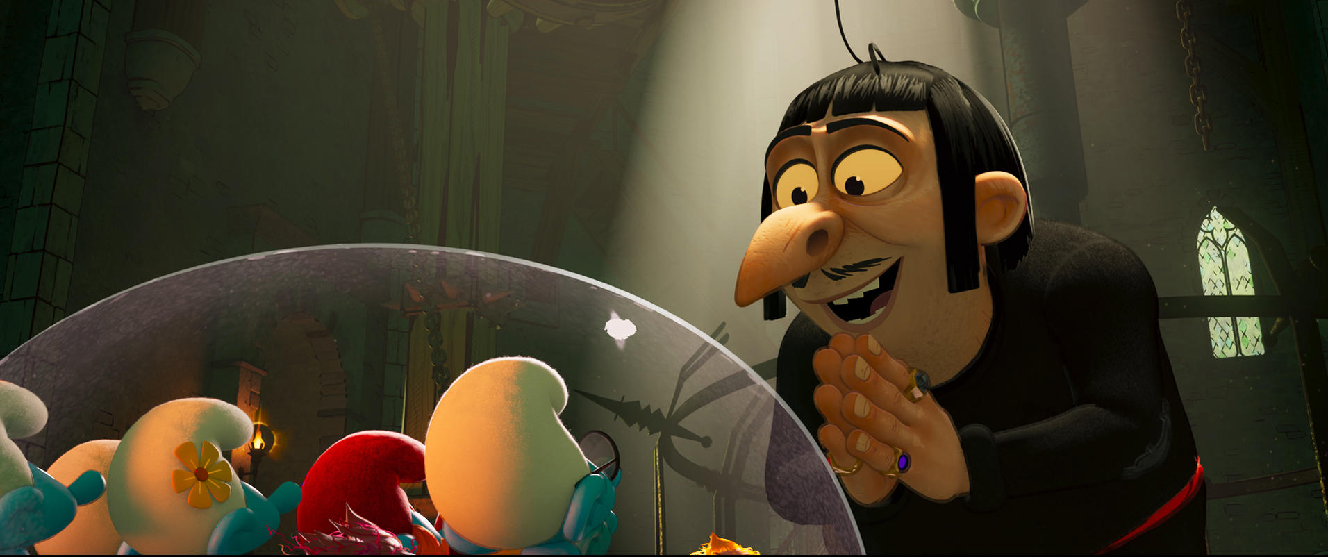 Gargamel grinst, die Hände gefaltet, und beobachtet Schlumpfe unter einer Glaskuppel. Die Szene spielt in einem dunklen, burgartigen Raum.