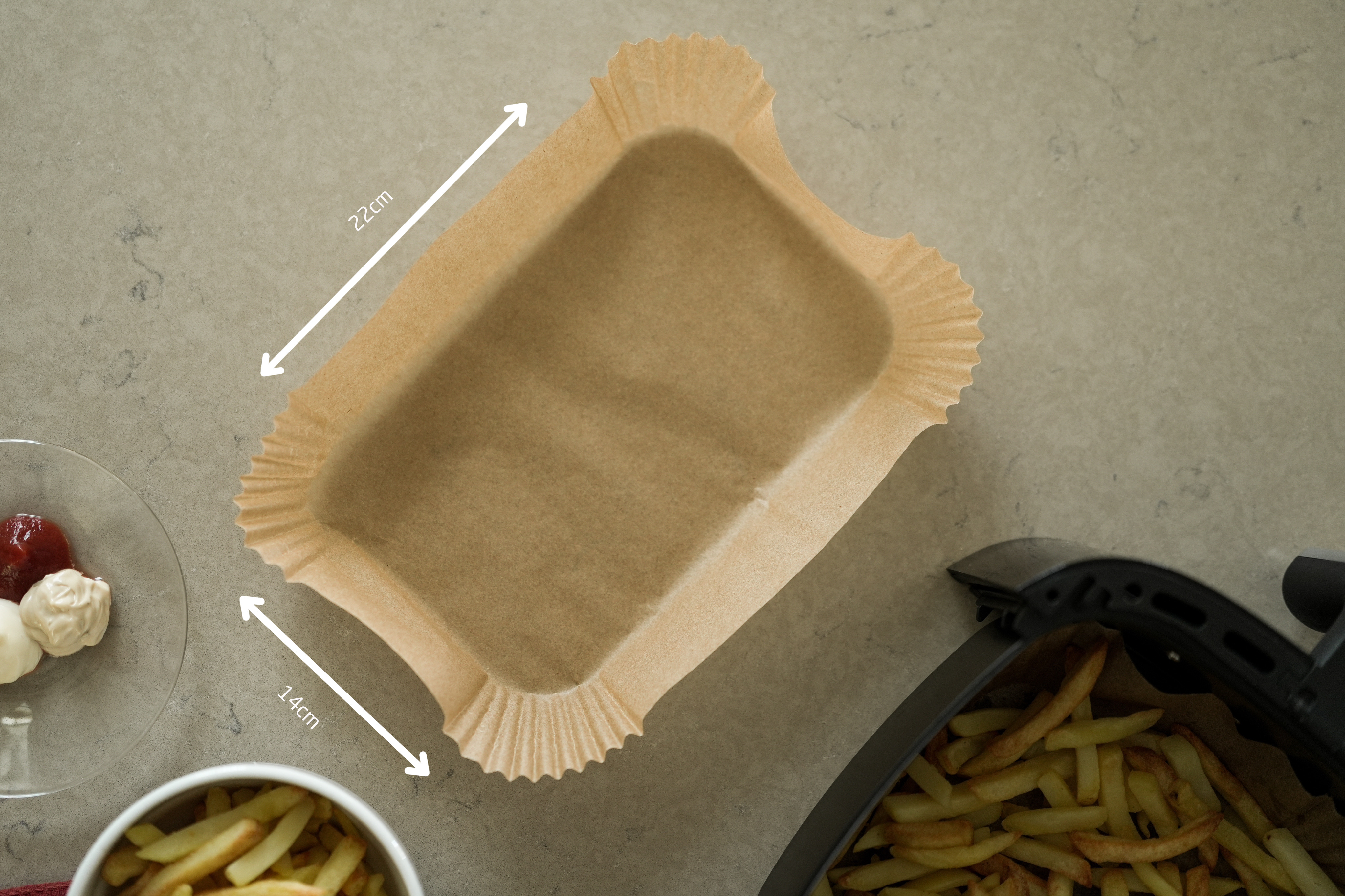 Eine Backpapier-Schale, eine Heißluftfritteuse mit Pommes, eine Schüssel Pommes und ein kleines Glas mit Saucen.