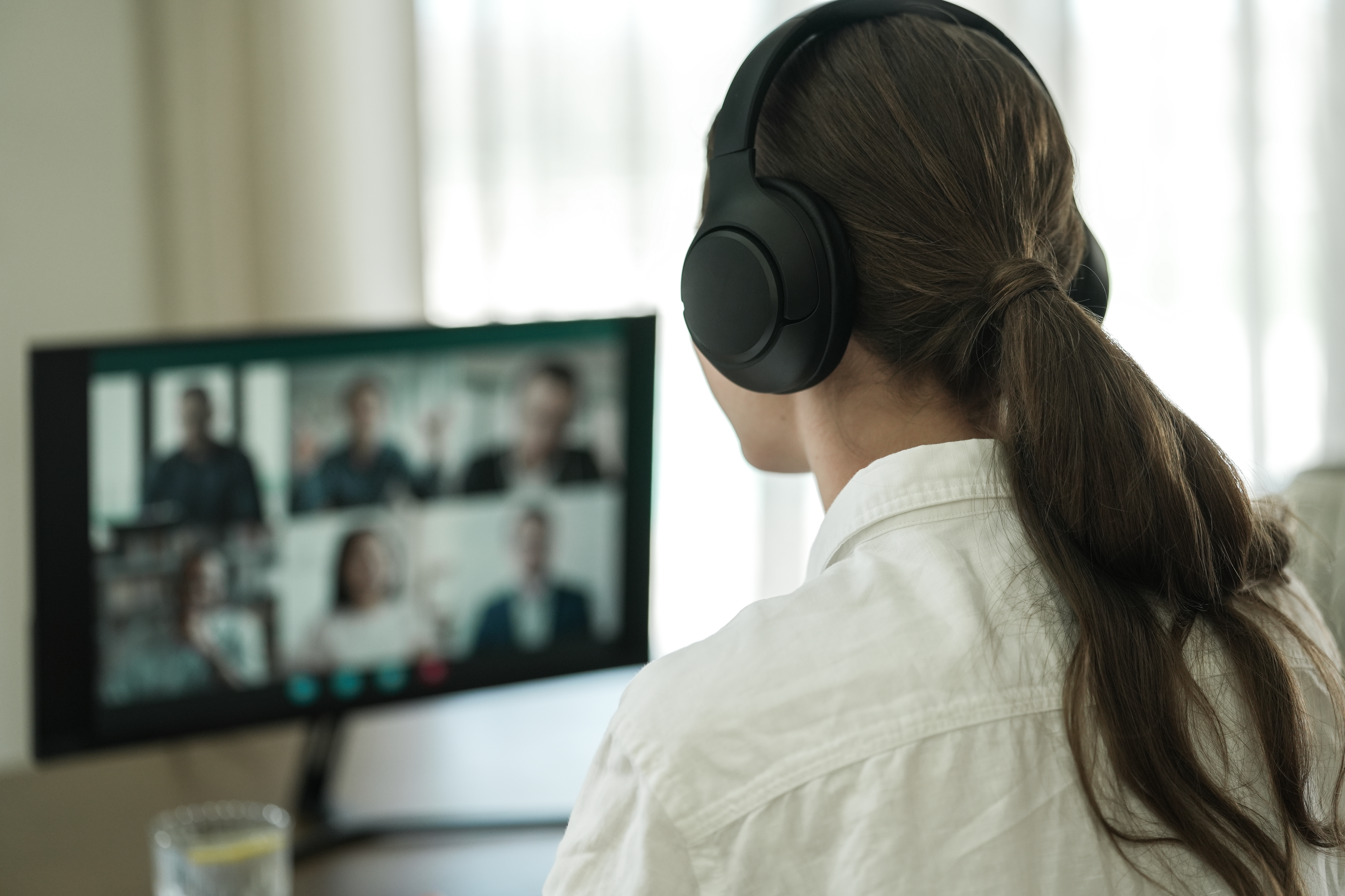 Une personne portant un casque assiste à un appel vidéo. L'écran affiche d'autres participants. L'accent est mis sur le dos de la personne.