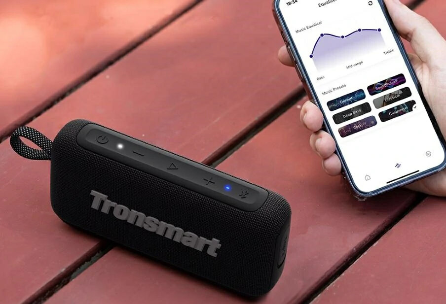 Czarny głośnik Tronsmart i telefon z aplikacją equalizera muzyki na drewnianej powierzchni. Dłoń trzymająca telefon.