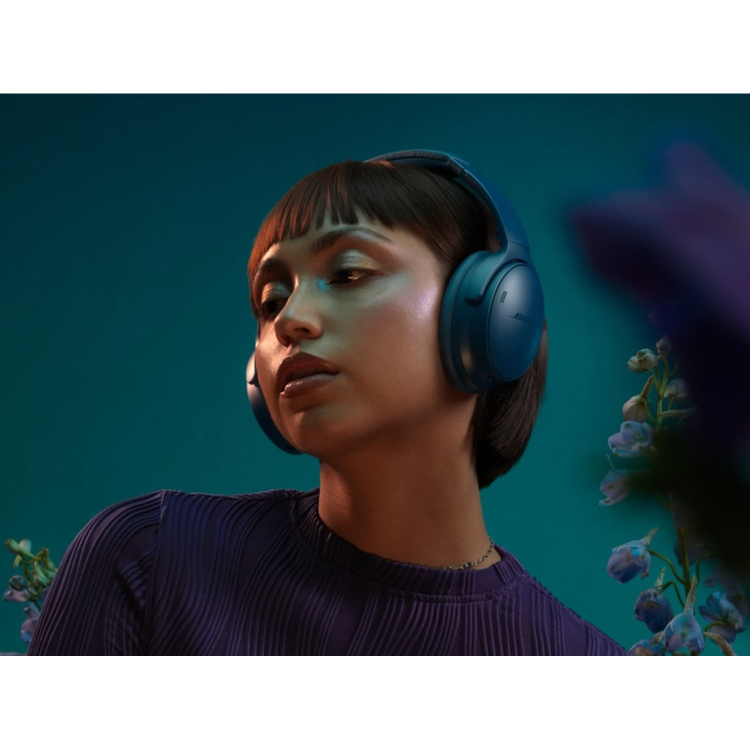 Vrouw met blauwe koptelefoon, kijkt naar links. Ze draagt een paarse blouse. Teal achtergrond met bloemen.