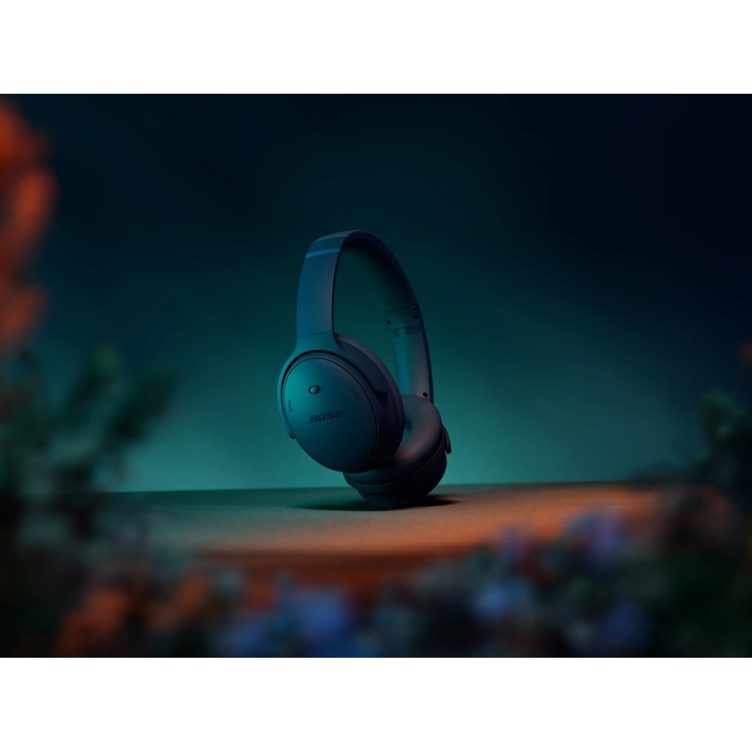 Donkerblauwe Bose-hoofdtelefoon op een houten oppervlak. Turquoise en oranje achtergrond met vage bloemen.
