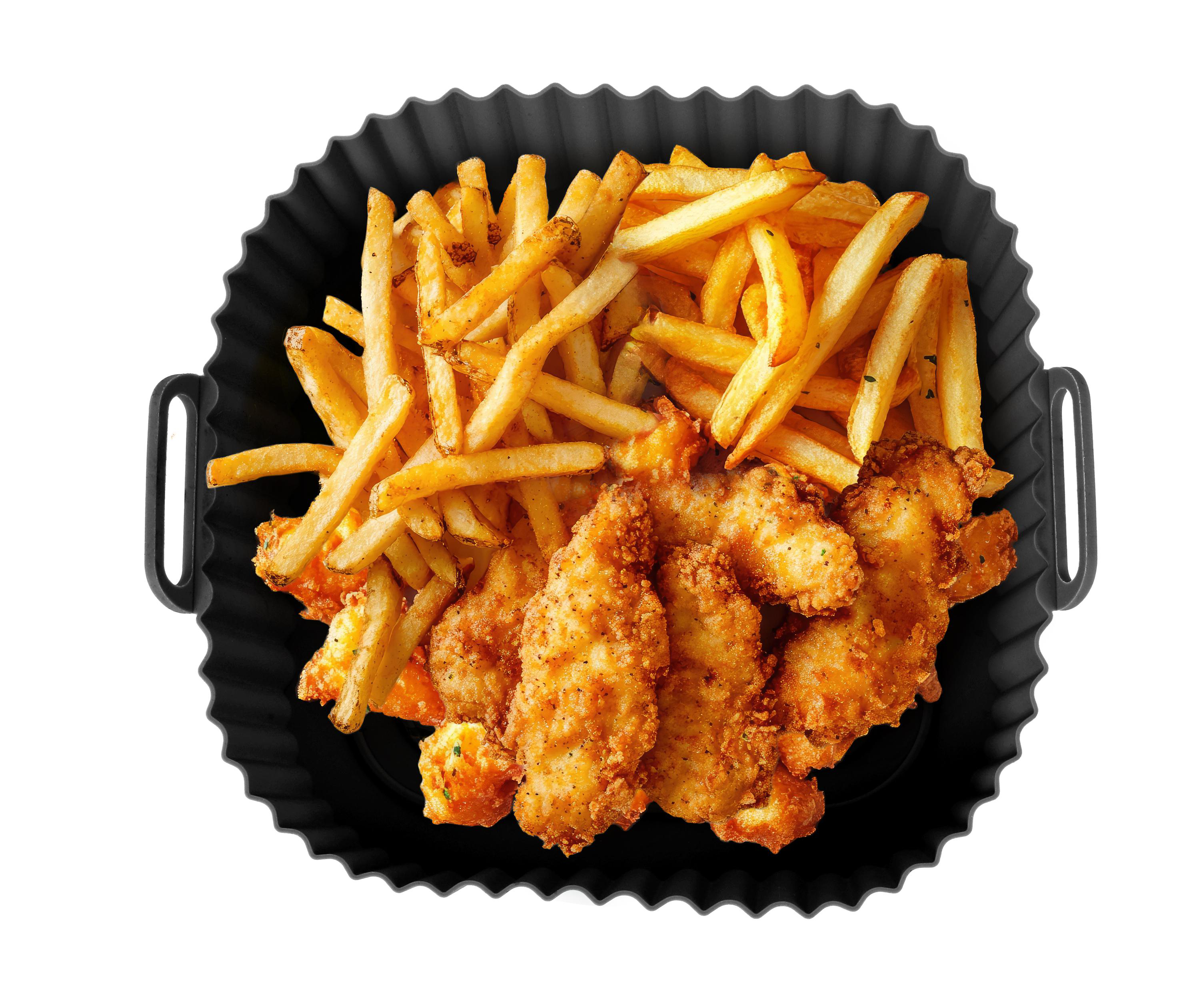 Draufsicht auf frittierte Hähnchenstücke und Pommes Frites in einer schwarzen Schale auf weißem Grund.