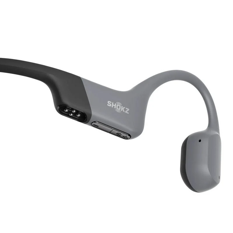 Auriculares Shokz grises y negros, parcialmente visibles, con el logotipo de la marca en el lateral. El diseño es elegante y moderno, sobre un fondo blanco.
