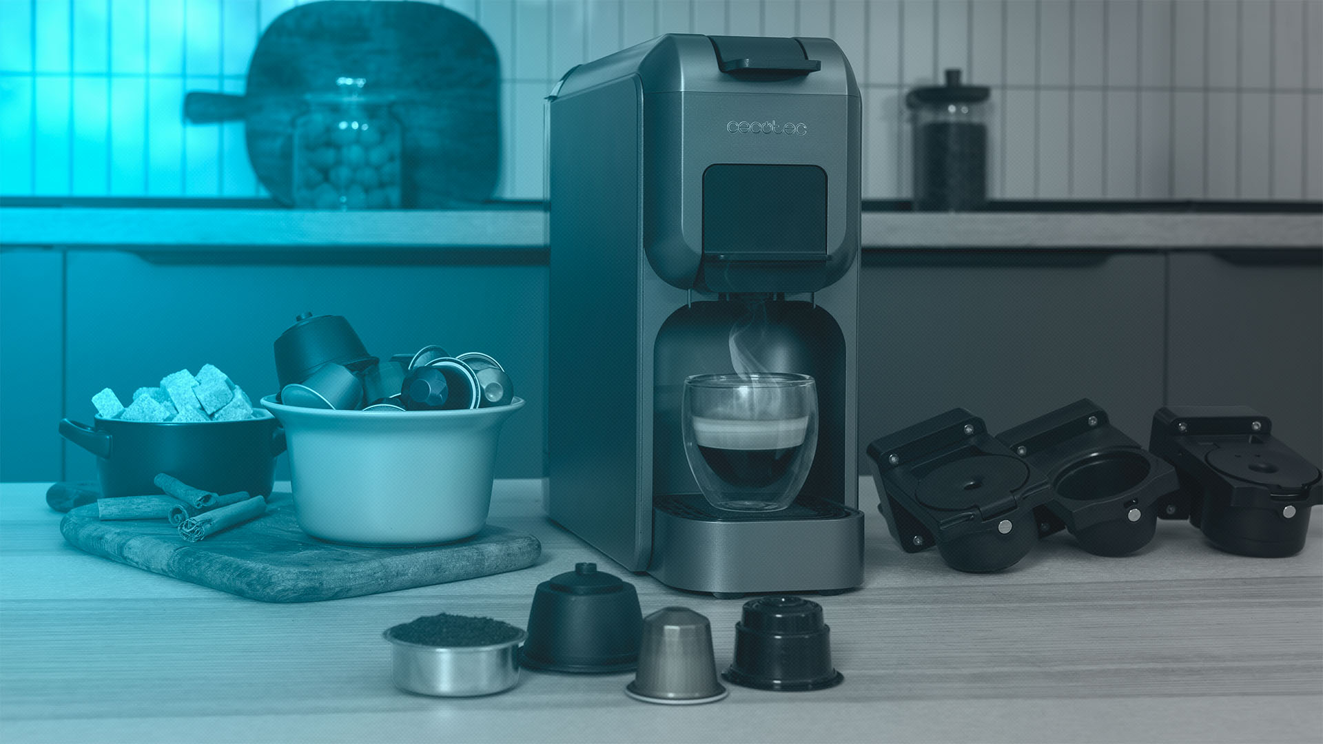Una cafetera con un vaso de café. Cápsulas de café, cubos de azúcar, palitos de canela y accesorios están al lado.