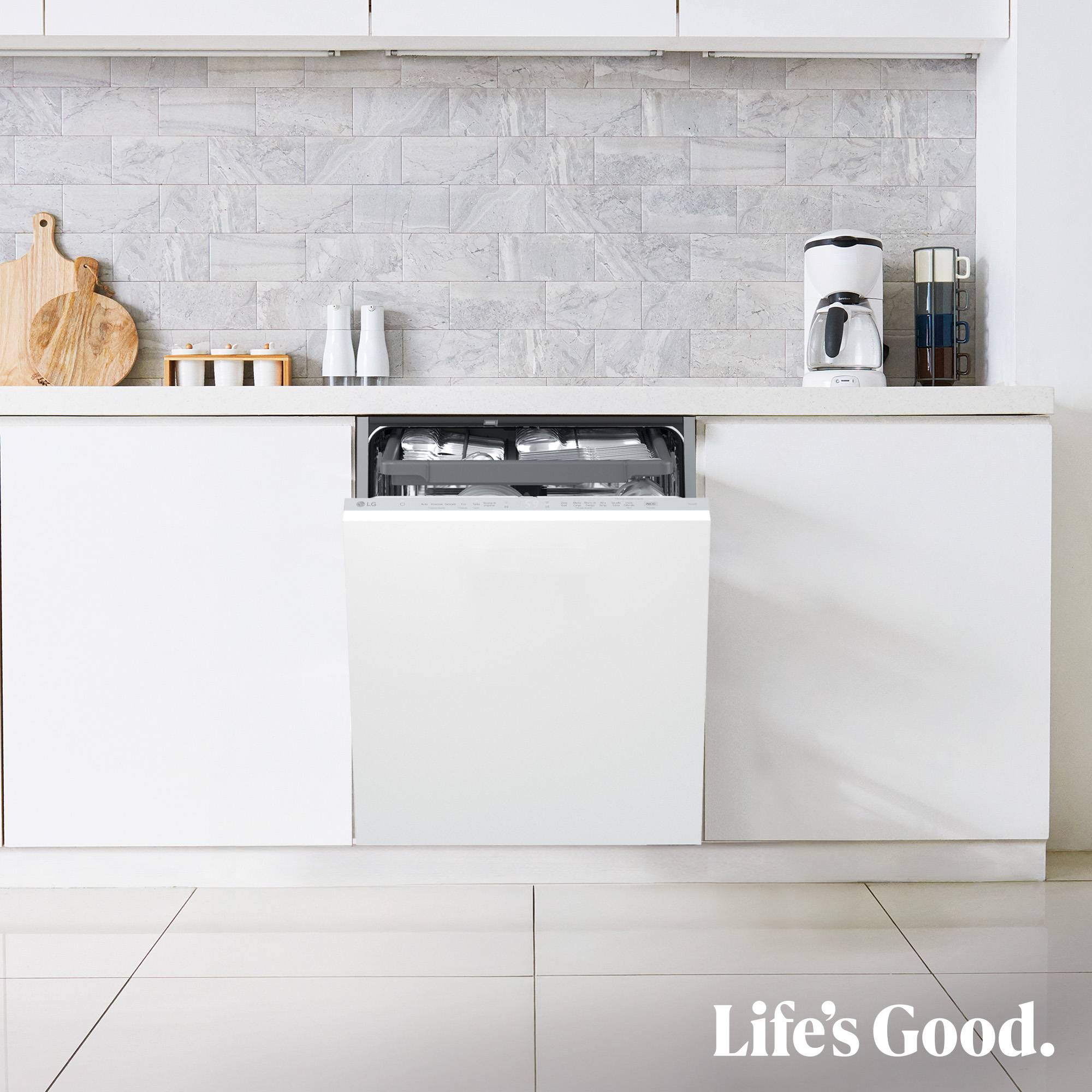 Una cocina blanca con lavavajillas abierto. Tablas de cortar, saleros, cafetera y tazas están en la encimera.