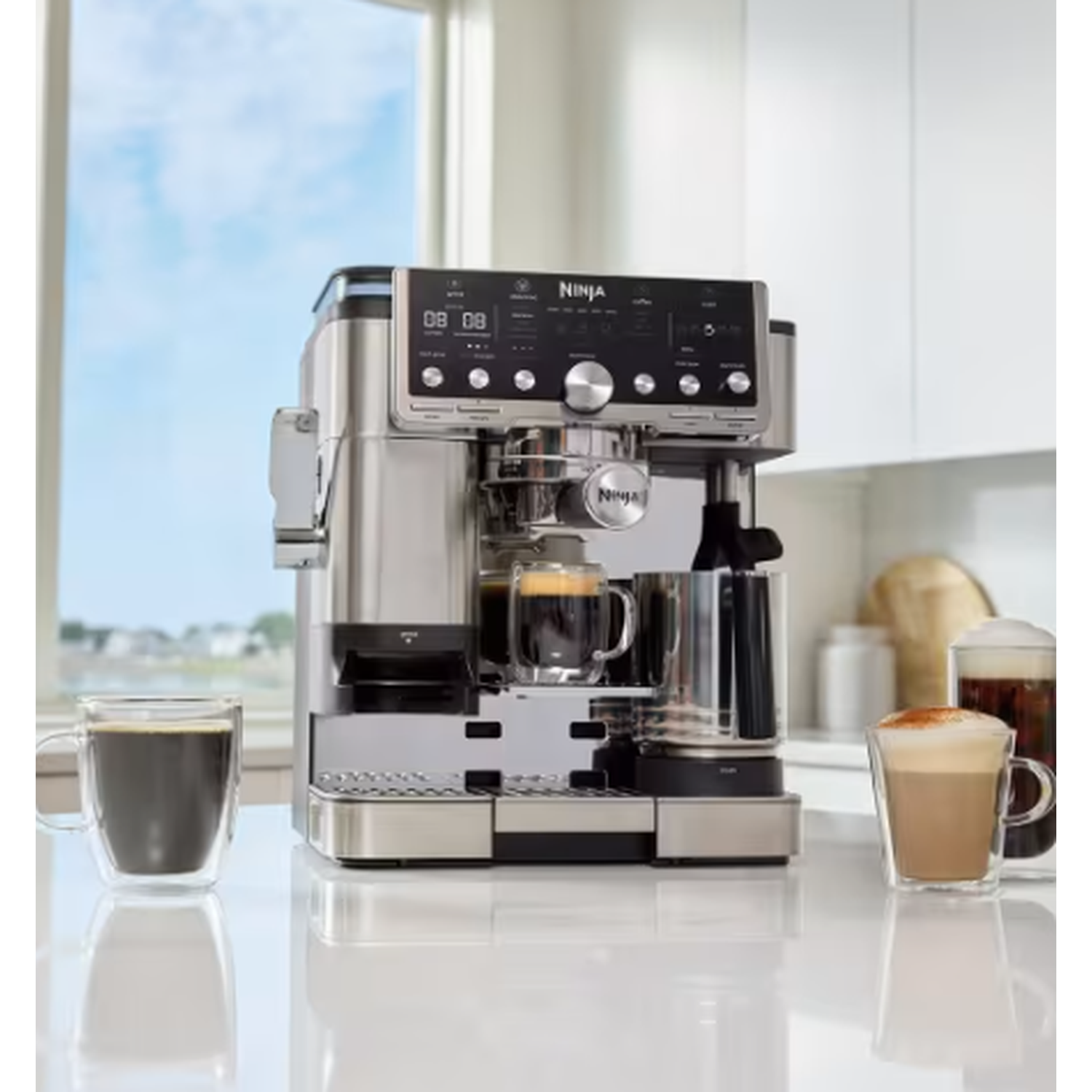 Een Ninja koffiezetapparaat met een dubbelwandige glazen koffiemok op een aanrecht. Een raam met blauwe lucht op de achtergrond.