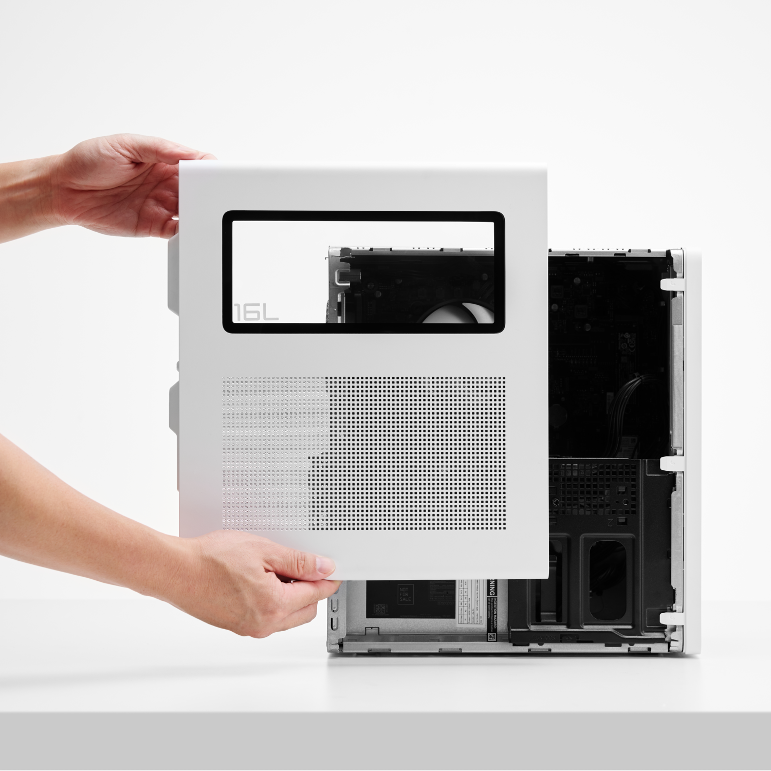 Manos sosteniendo un panel blanco de caja de ordenador, junto a una caja de ordenador abierta. El panel tiene un rectángulo negro y pequeños agujeros.