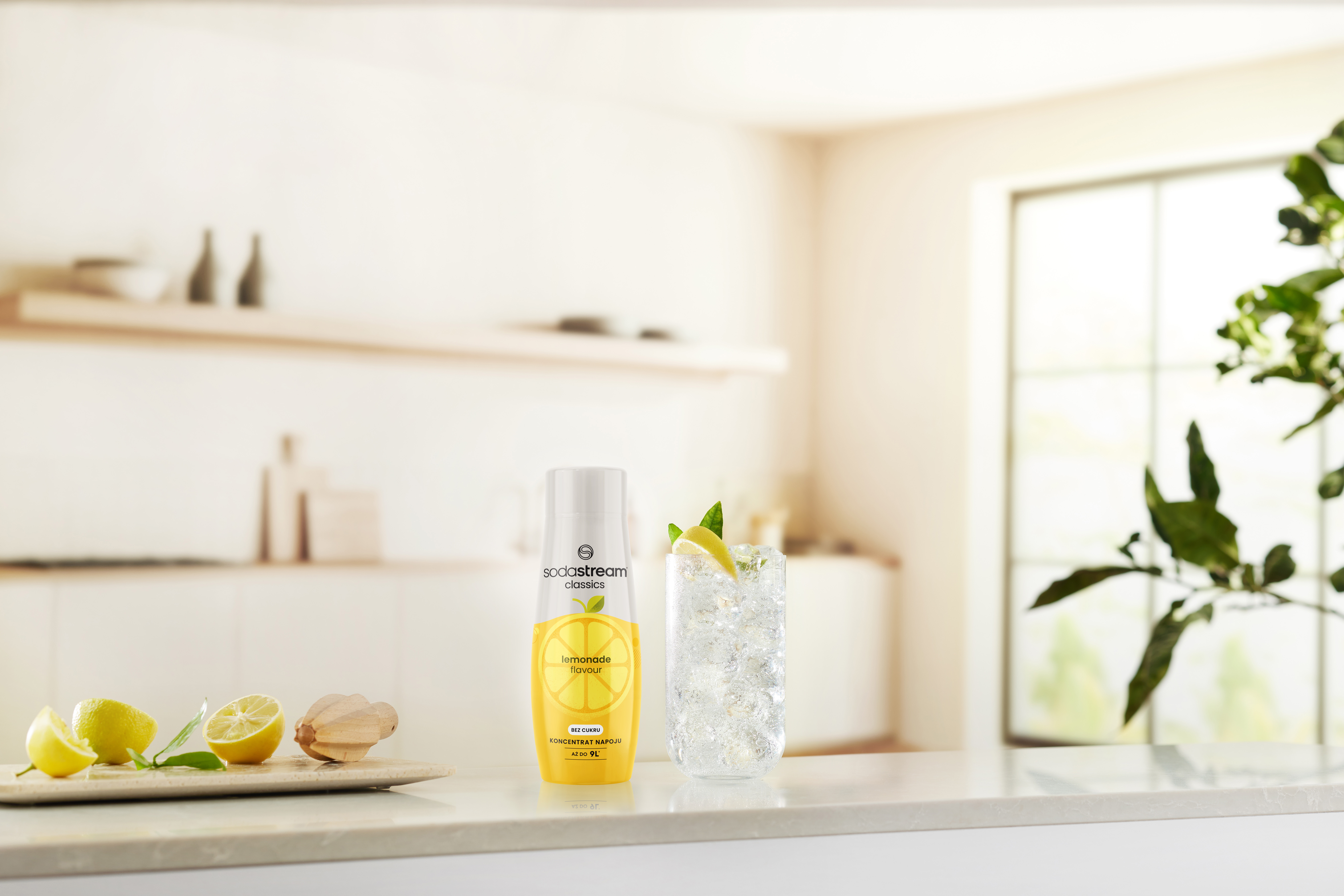 Scena kuchenna z szklanką wody z lodem i cytryną, butelką i cytrynami na blacie.