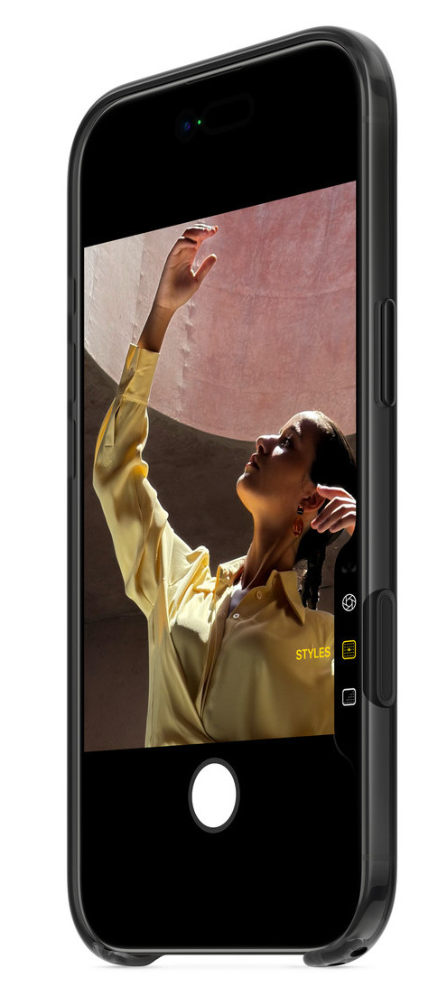 Kobieta w żółtej koszuli sięga w górę, uchwycona na ekranie telefonu. Telefon jest czarny z przezroczystym etui.